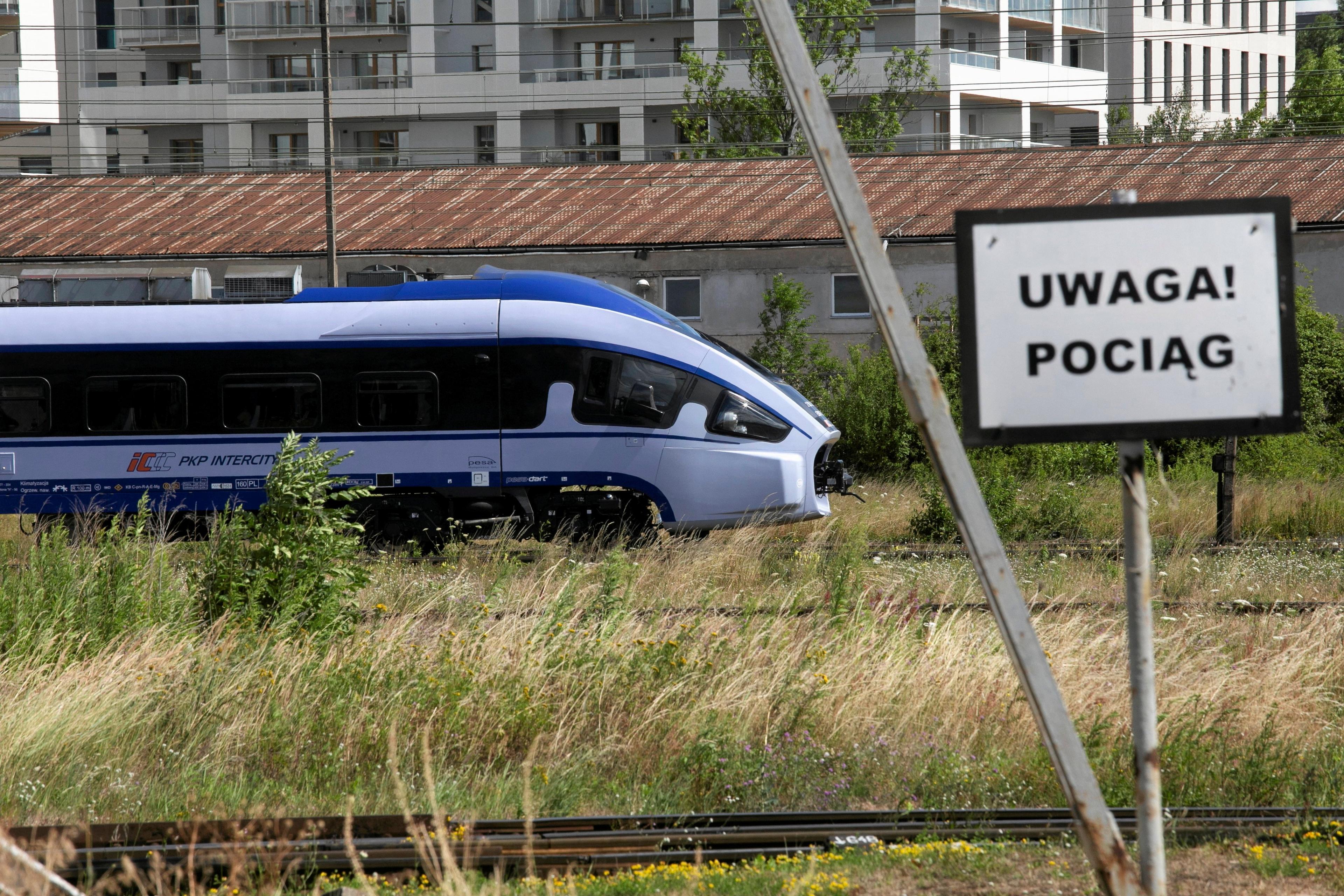 nowy skład PKP Intercity jedzie przez zieleń, na pierwszym planie znak z napisem Uwaga Pociąg