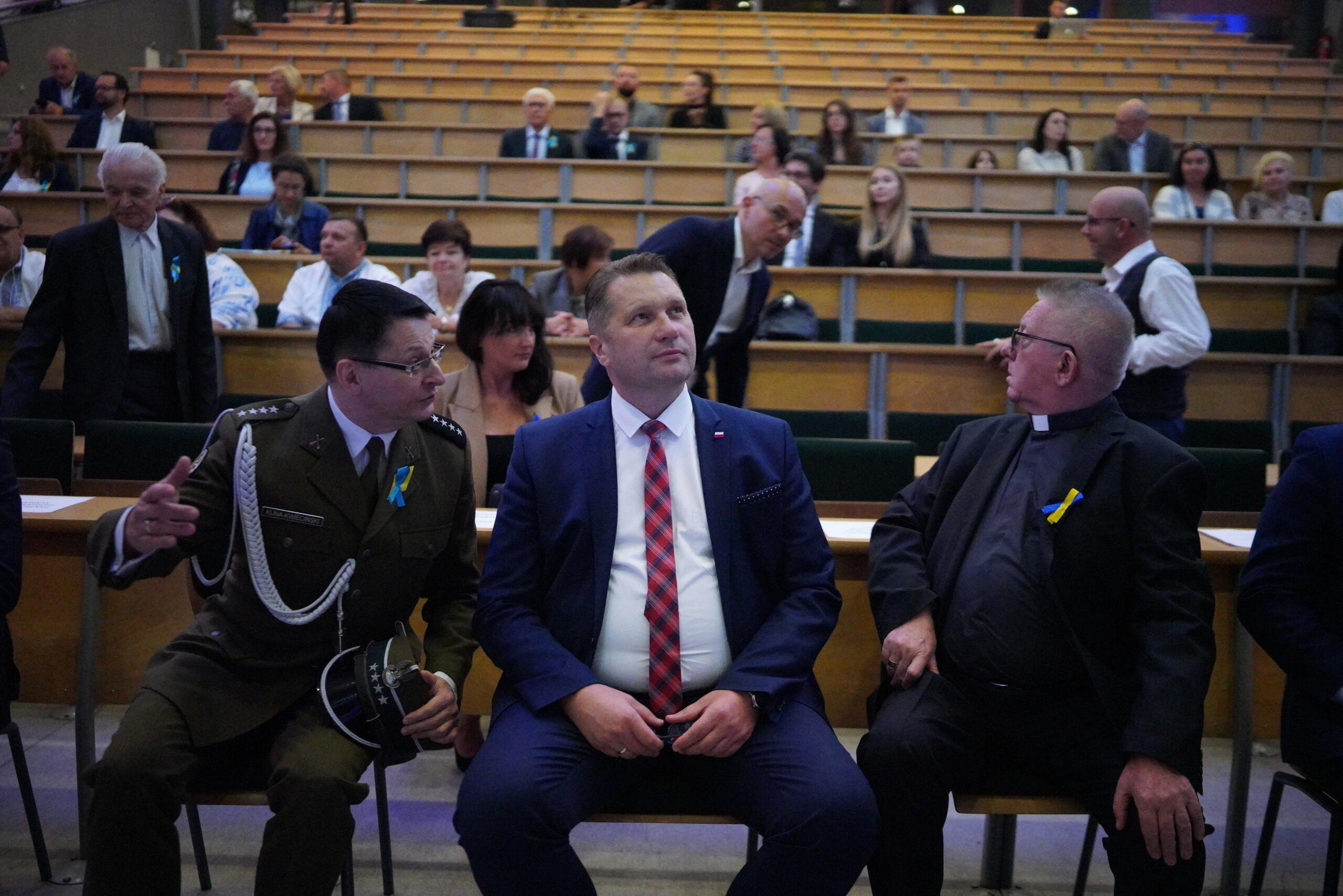 Minister Czarnek siedzi w auli pomiędzy księdzem i wojskowym