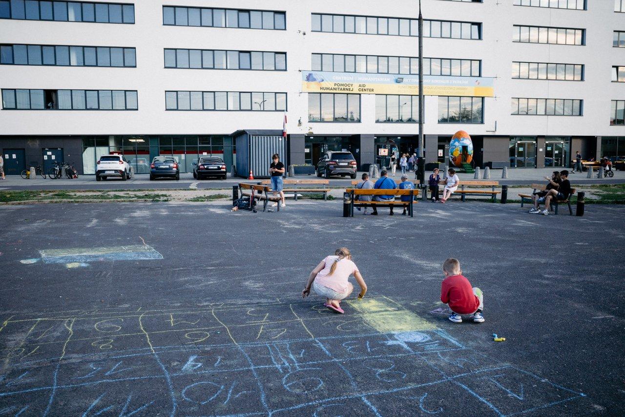 plac przed biurowcem, dzieci rysują kredą na asfalcie