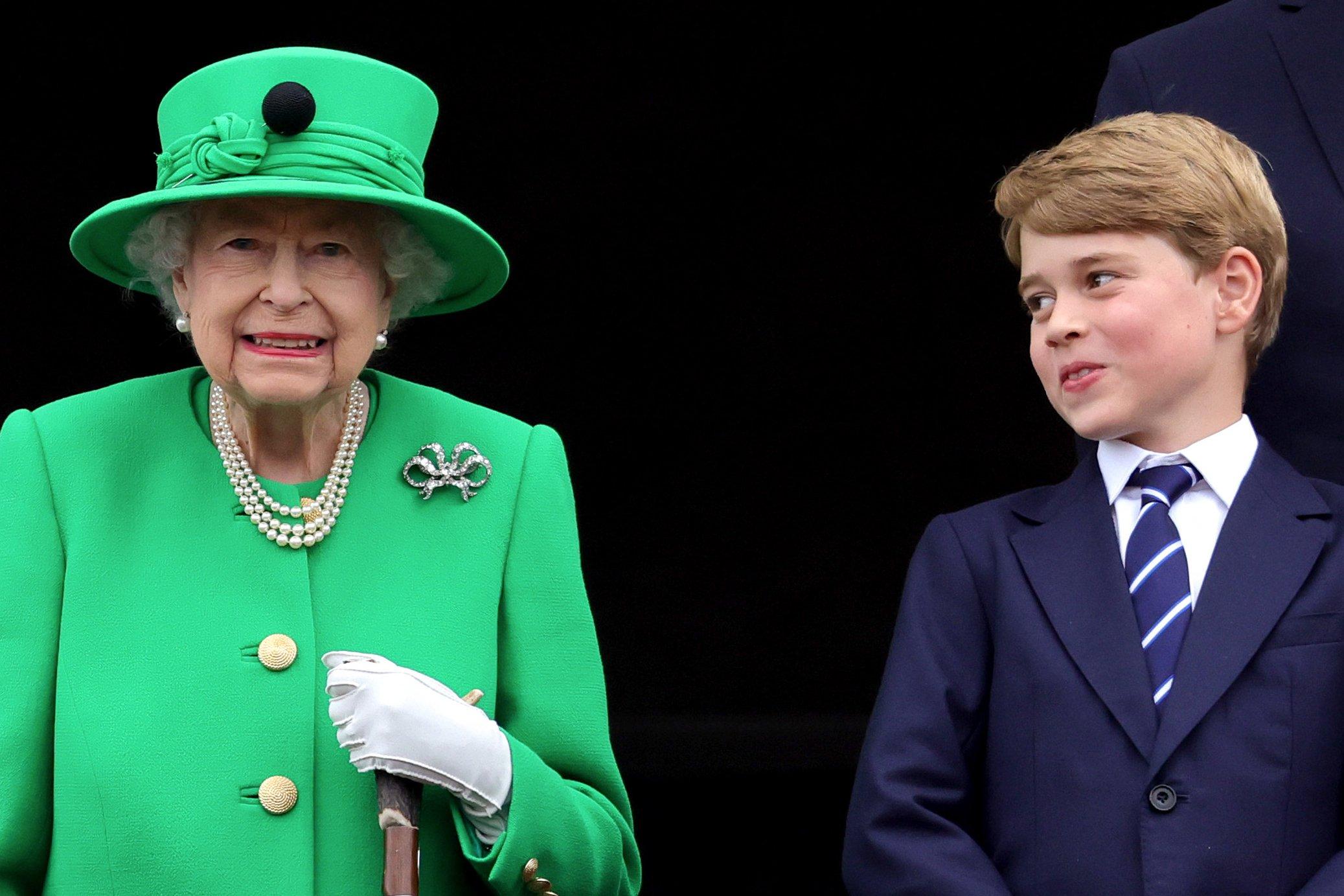 Królowa w zielonym płaszczyku i zielonym kapeluszu obok nastolatek w marynarce i w krawacie,. patrzy na nią z usmiechem