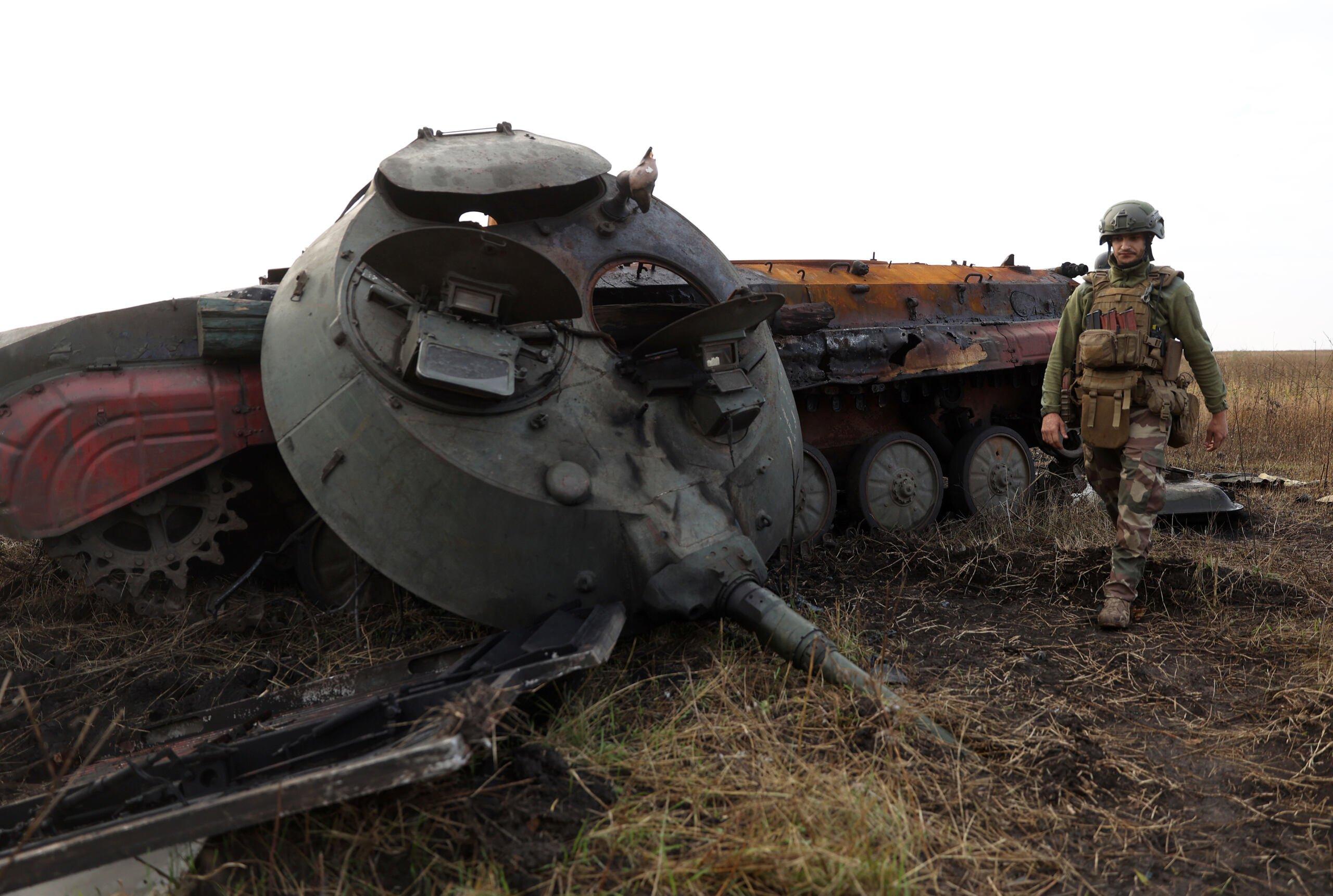 Ukraiński żołnierz idzie obok zniszczonego rosyjskiego pojazdu opancerzonego