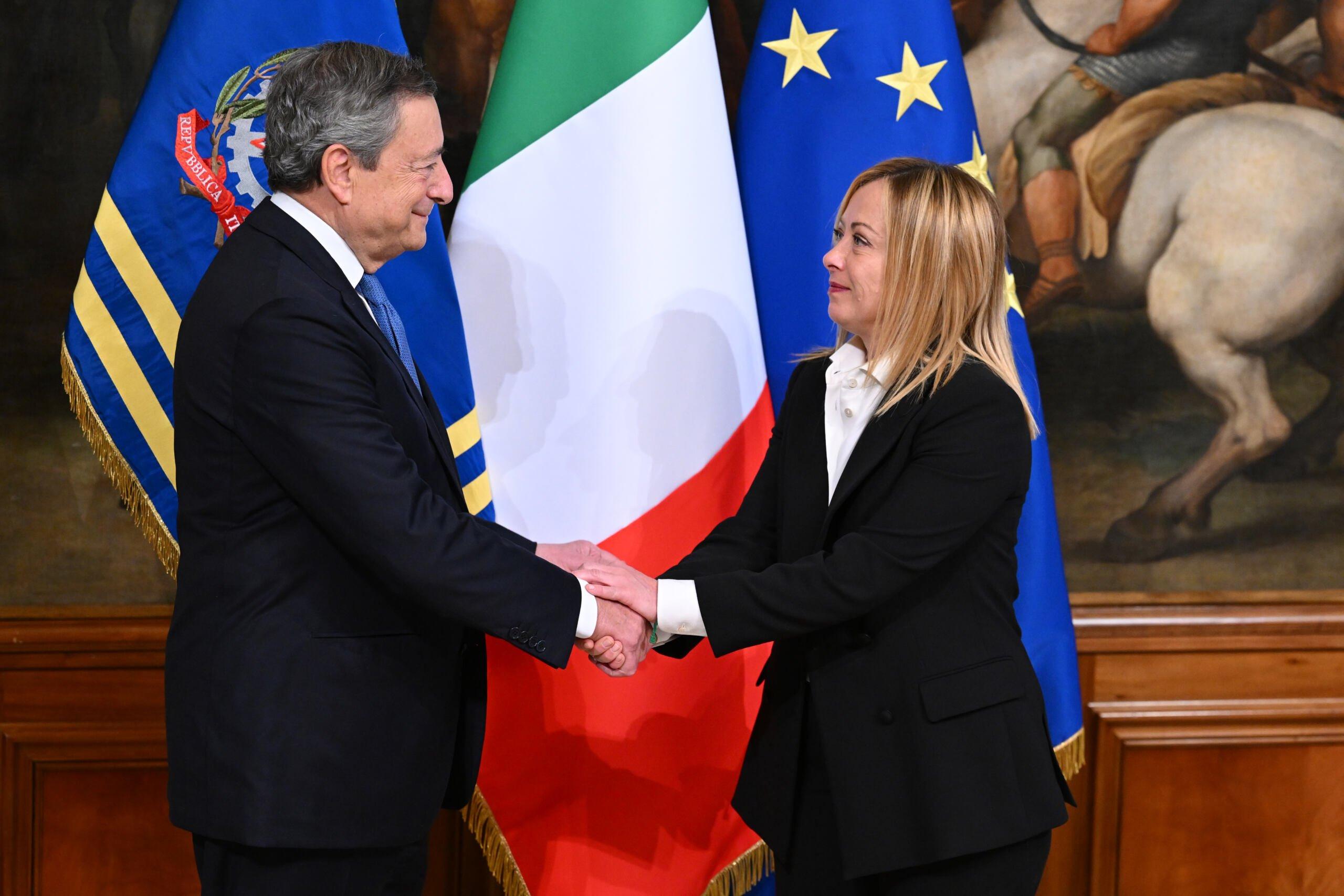 uścisk dłoni Meloni i Draghiego na tle flag Włoch i UE