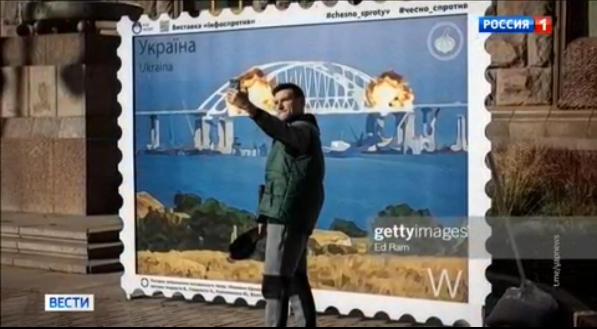 Mężczyzna robi sobie zdjęcie przez makietą znaczka z wybuchającym krymskim mostem