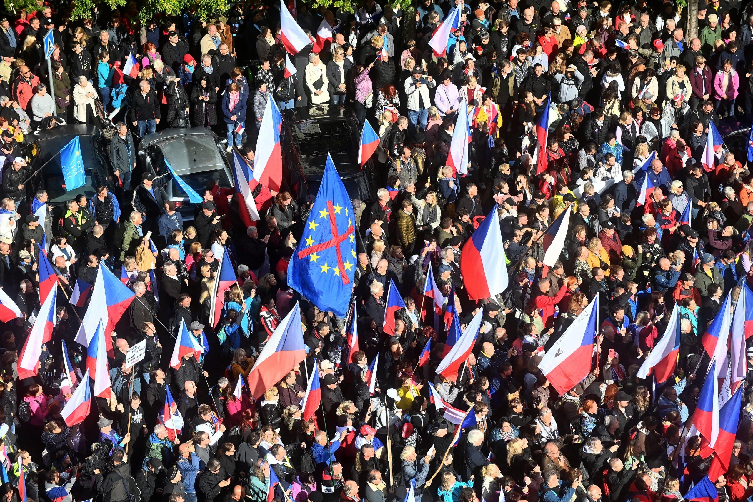 Tłum ludzi z czeskimi flagami, w centralnym miejscu transaprent z przekroślonymi gwiazdkami Unii Europejskiej
