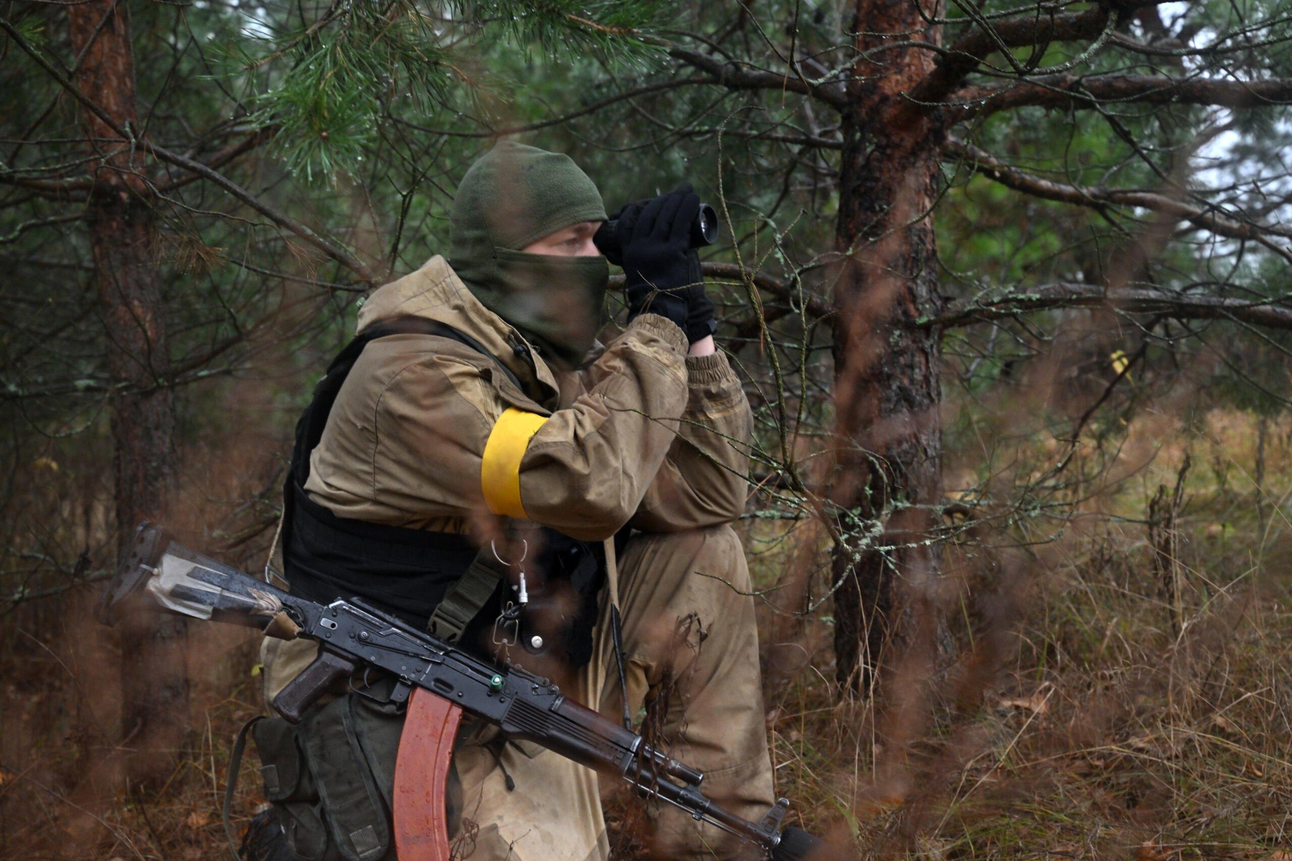 Żołnierz z ukraińską żółtą opaską patrzy przez lornetkę
