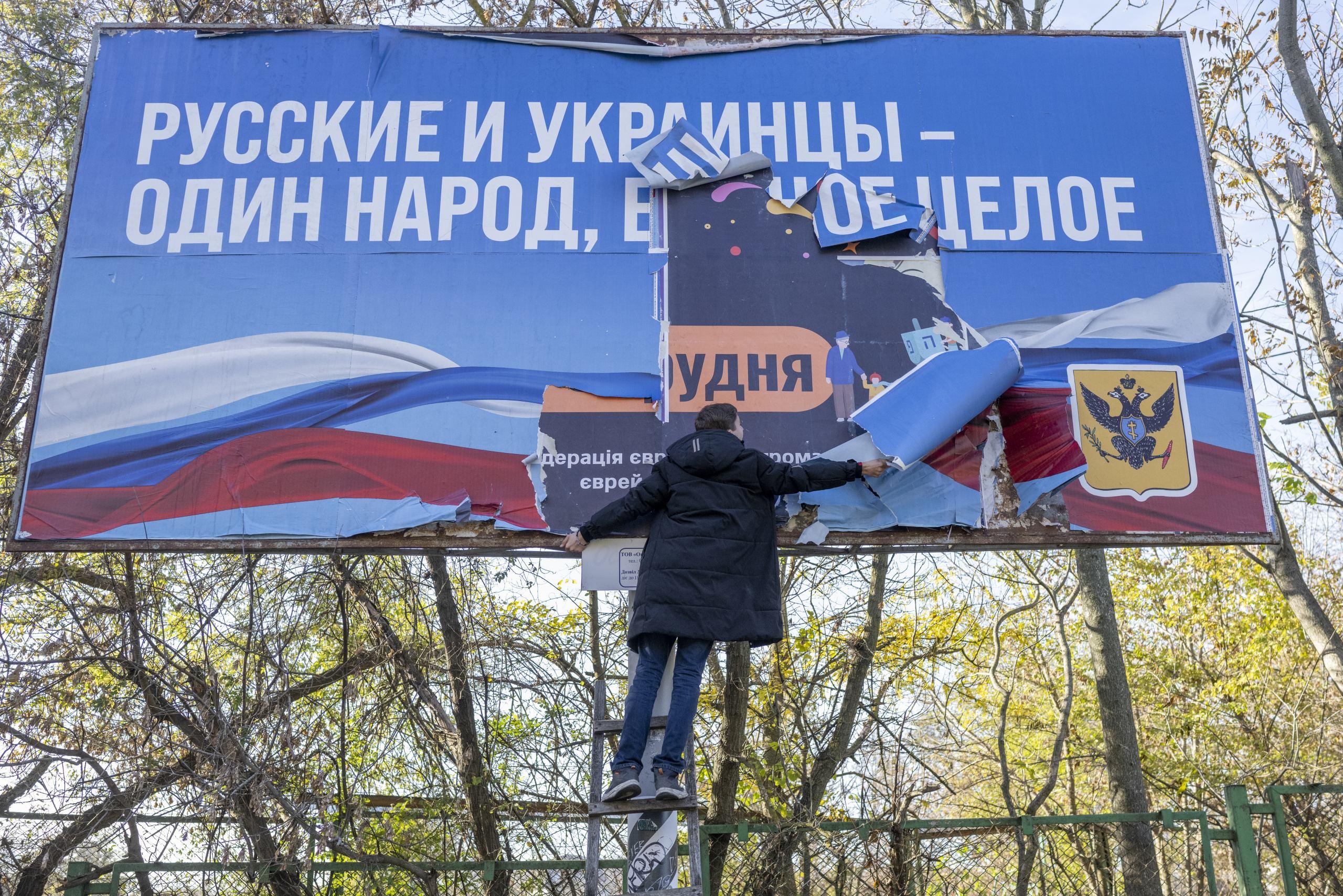 Człowiek zrywa wielki billboard z rosyjskim napisem: Rosjanie i Ukraińcy - jeden naród"