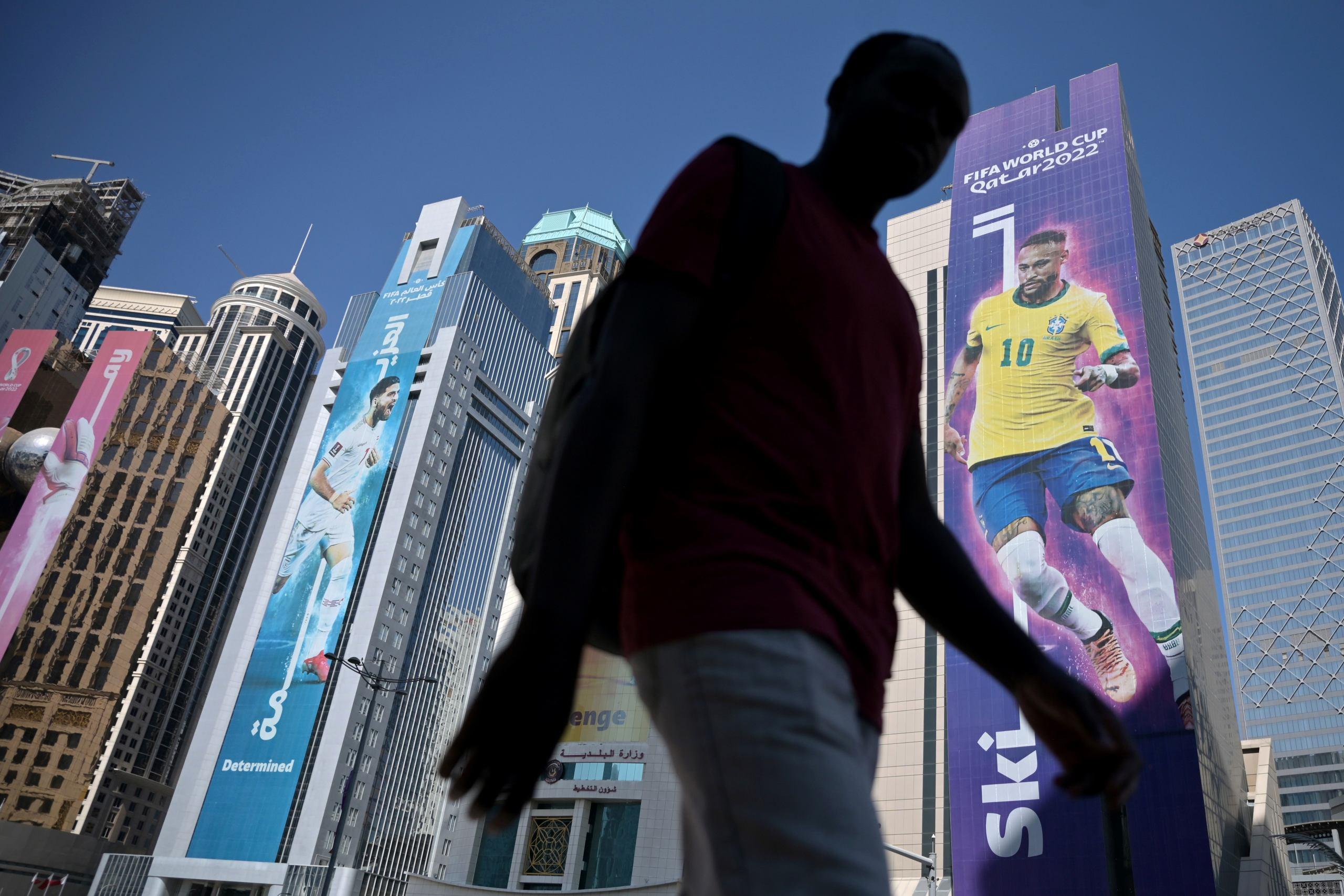 A man walks past banners of football players displayed on buildings along the Corniche in Doha on November 17, 2022, ahead of the Qatar 2022 World Cup football tournament. (Photo by Raul ARBOLEDA / AFP)
