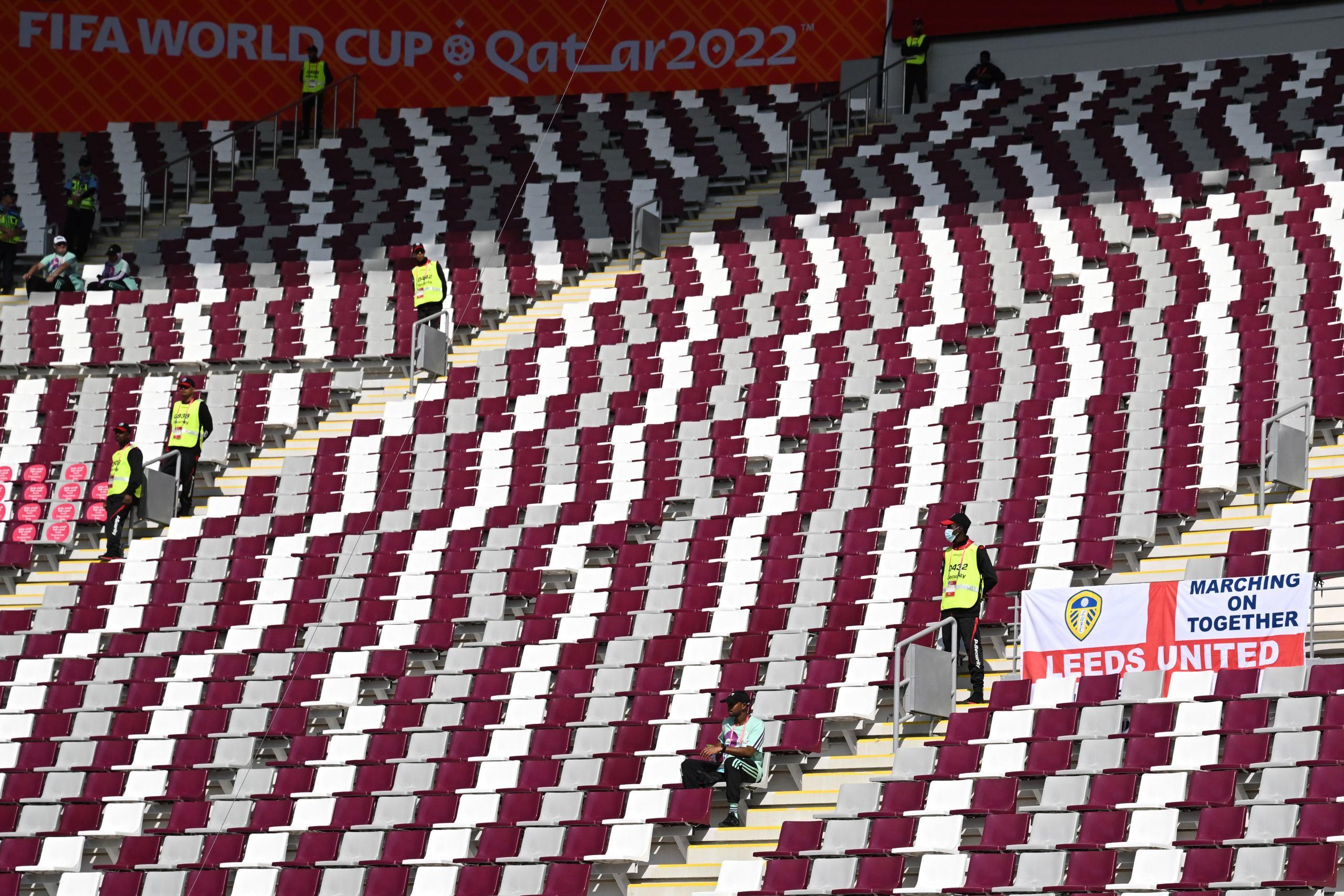 A member of security personnel stands guard next to a Leeds United banner amid empty seats before the start of the Qatar 2022 World Cup Group B football match between England and Iran at the Khalifa International Stadium in Doha on November 21, 2022. (Photo by Paul ELLIS / AFP)