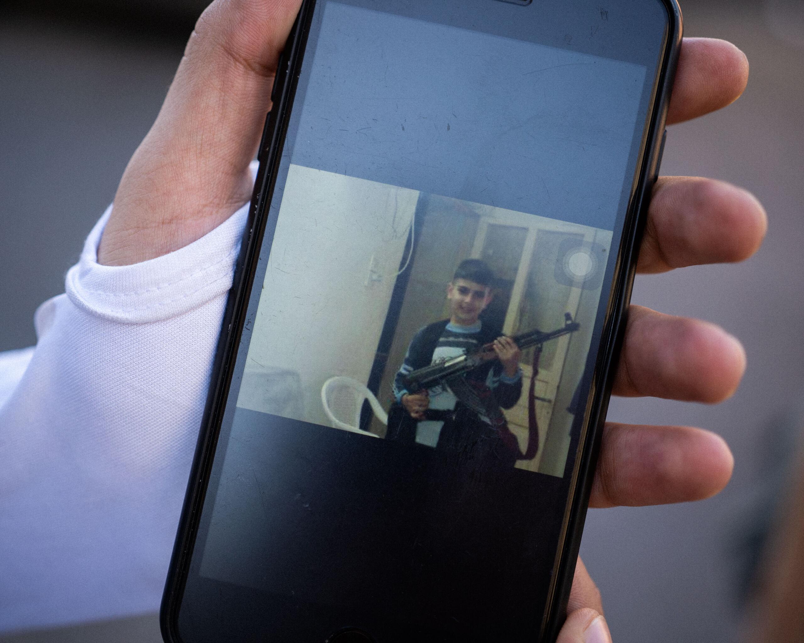 ekran telefonu ze zdjeciem uśmiechniętego chłopca z karabinem