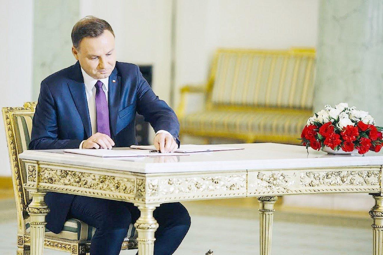 Prezydent siedzi przy zabytkowym biurku i podpisuje piórem wiecznym papiery