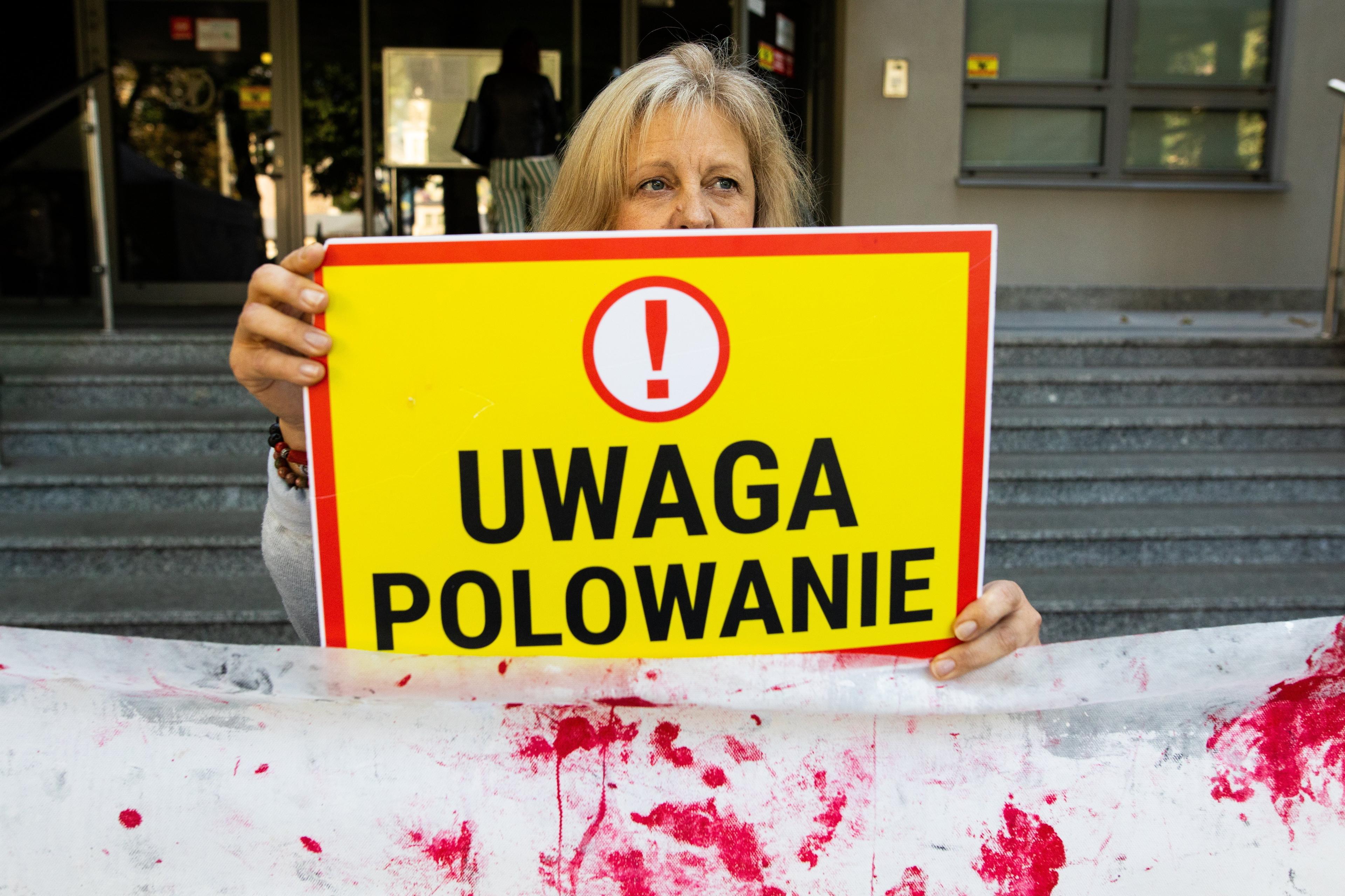 Kobieta trzyma tabliczkę z napisem "Uwaga Polowanie", poniżej zakrwawione prześcieradło