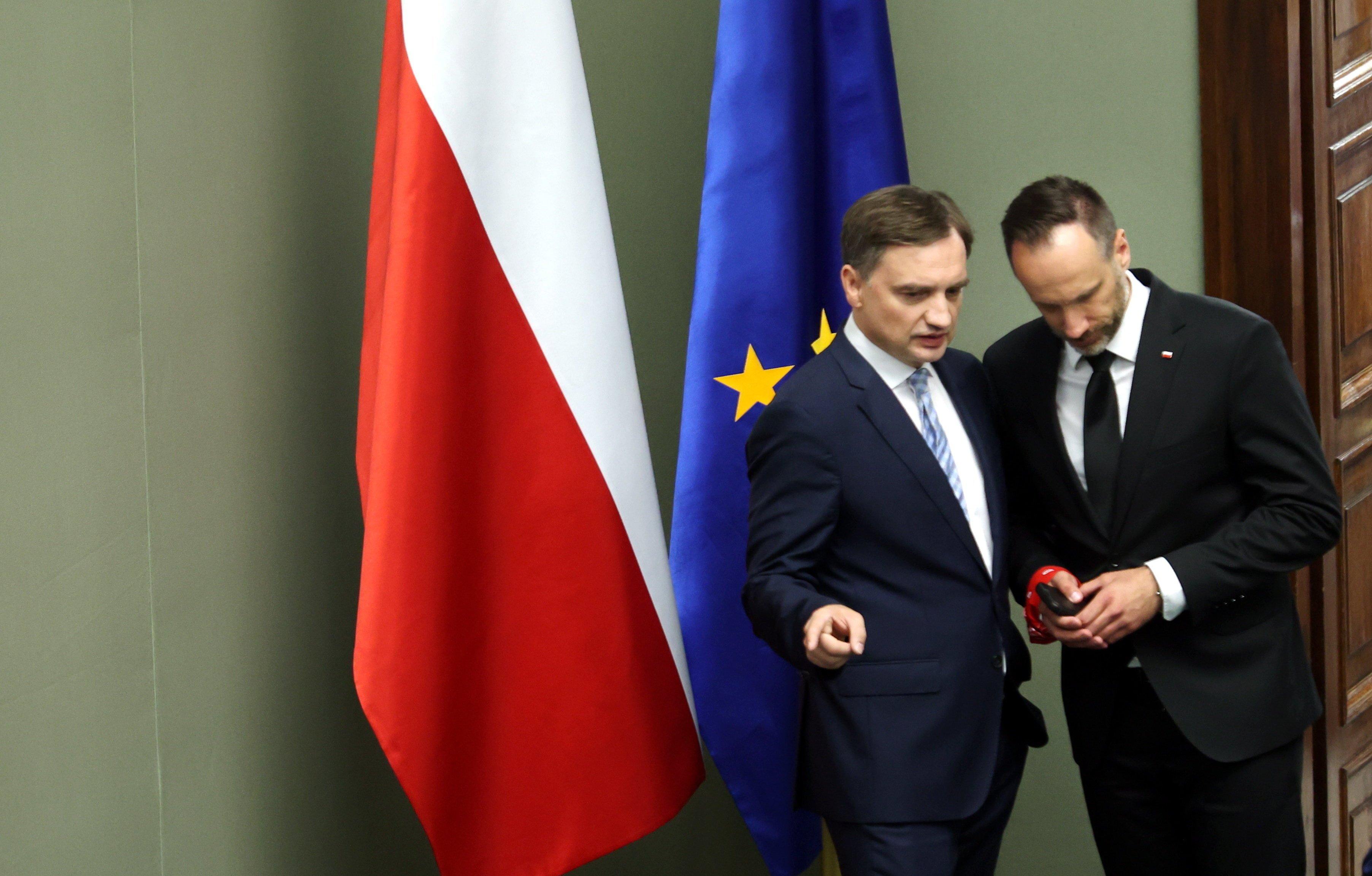 Dwaj mężczyźni w garniturach, Zbigniew Ziobro i Janusz Kowalski stoją w Sejmie na tle flag Polski i Unii Europejskiej