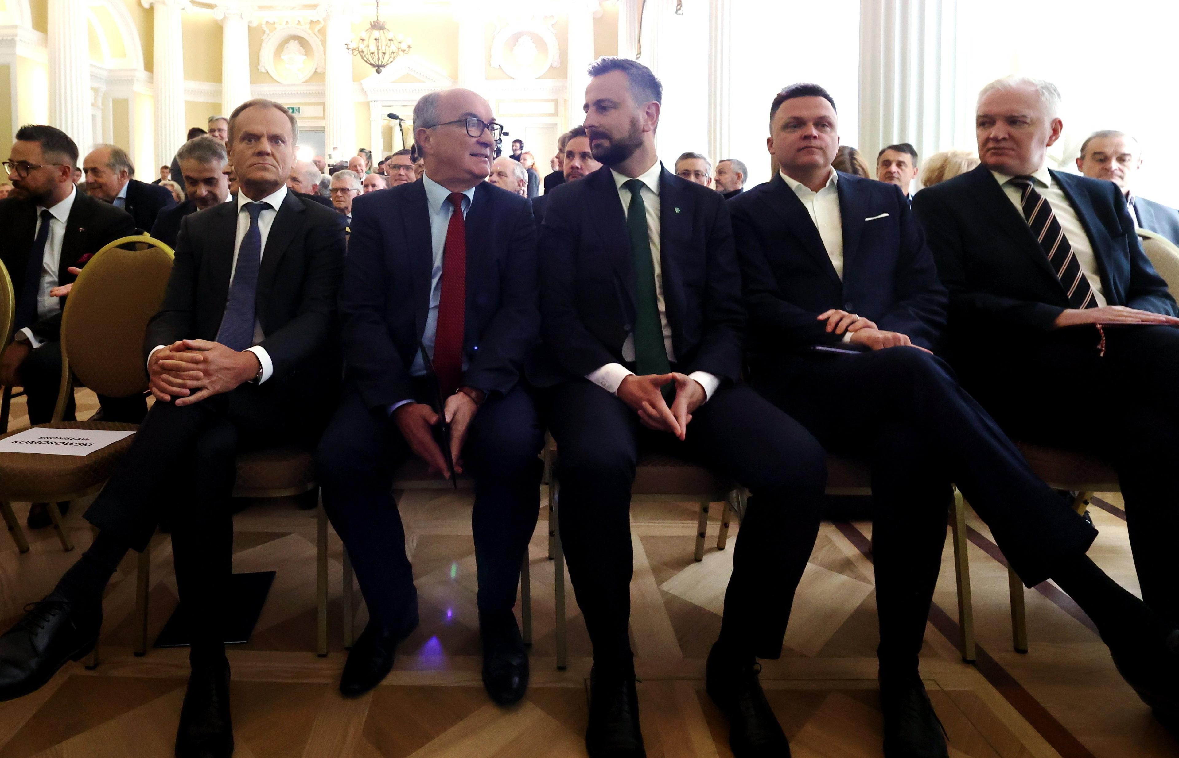 Liderzy opozycji - Donald Tusk, Włodzimierz Czarzasty, Władysław Kosiniak-Kamysz, Szymon Hołownia, ubrani w garnitury, siedzą w rzędzie na krzesłach w dużej sali