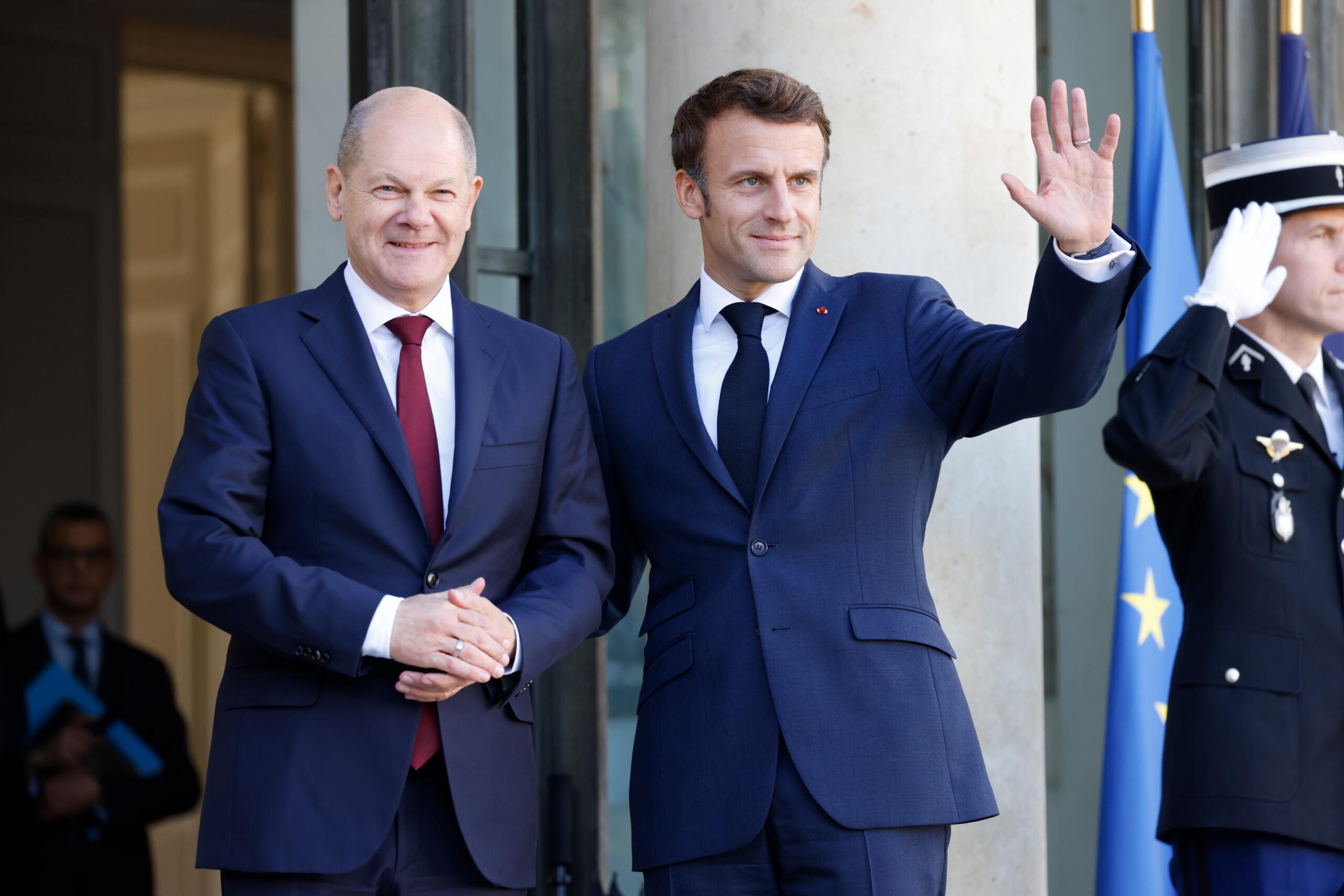Macron macha ręką stojąc obok Scholza