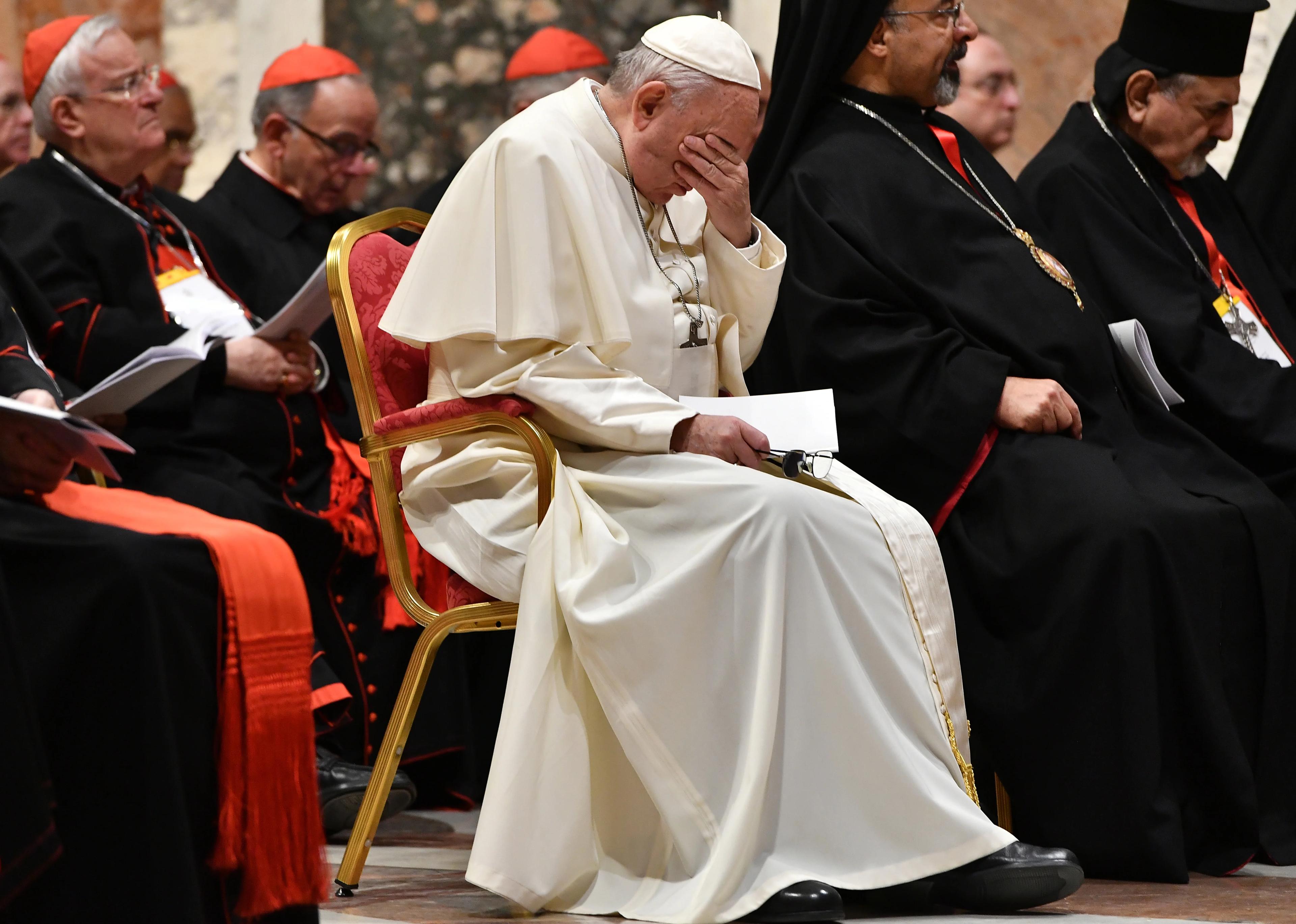 papież siedzi w otoczeniu biskupów, zasłaniając twarz rękoma