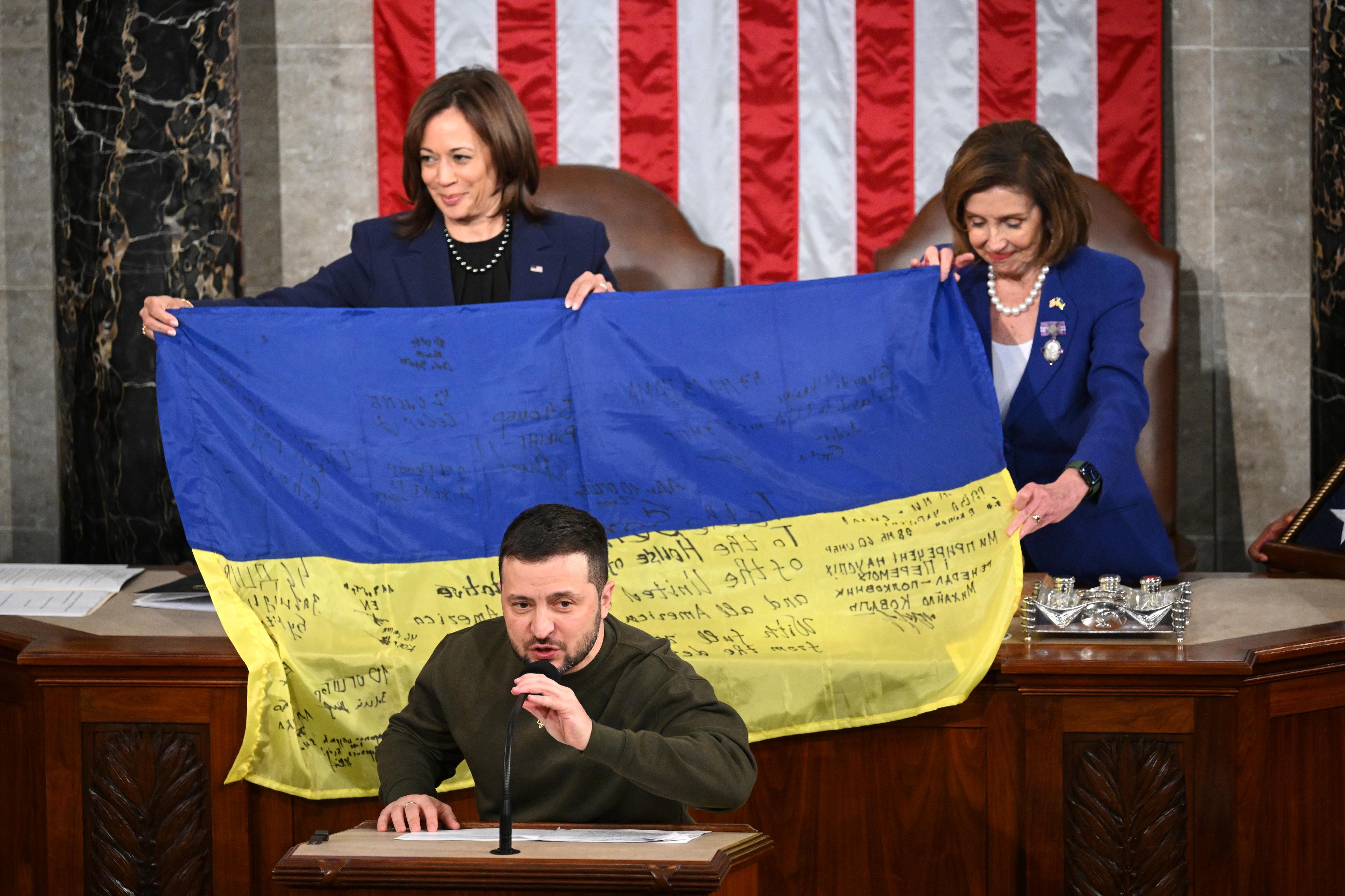 Ukraine's President Volodymyr Zelensky speaks after giving a Ukrainian national flag to US House Speaker Nancy Pelosi (D-CA) and US Vice President Kamala Harris (L) during his address the US Congress at the US Capitol in Washington, DC on December 21, 2022. - Zelensky is in Washington to meet with US President Joe Biden and address Congress -- his first trip abroad since Russia invaded in February. (Photo by Mandel NGAN / AFP)