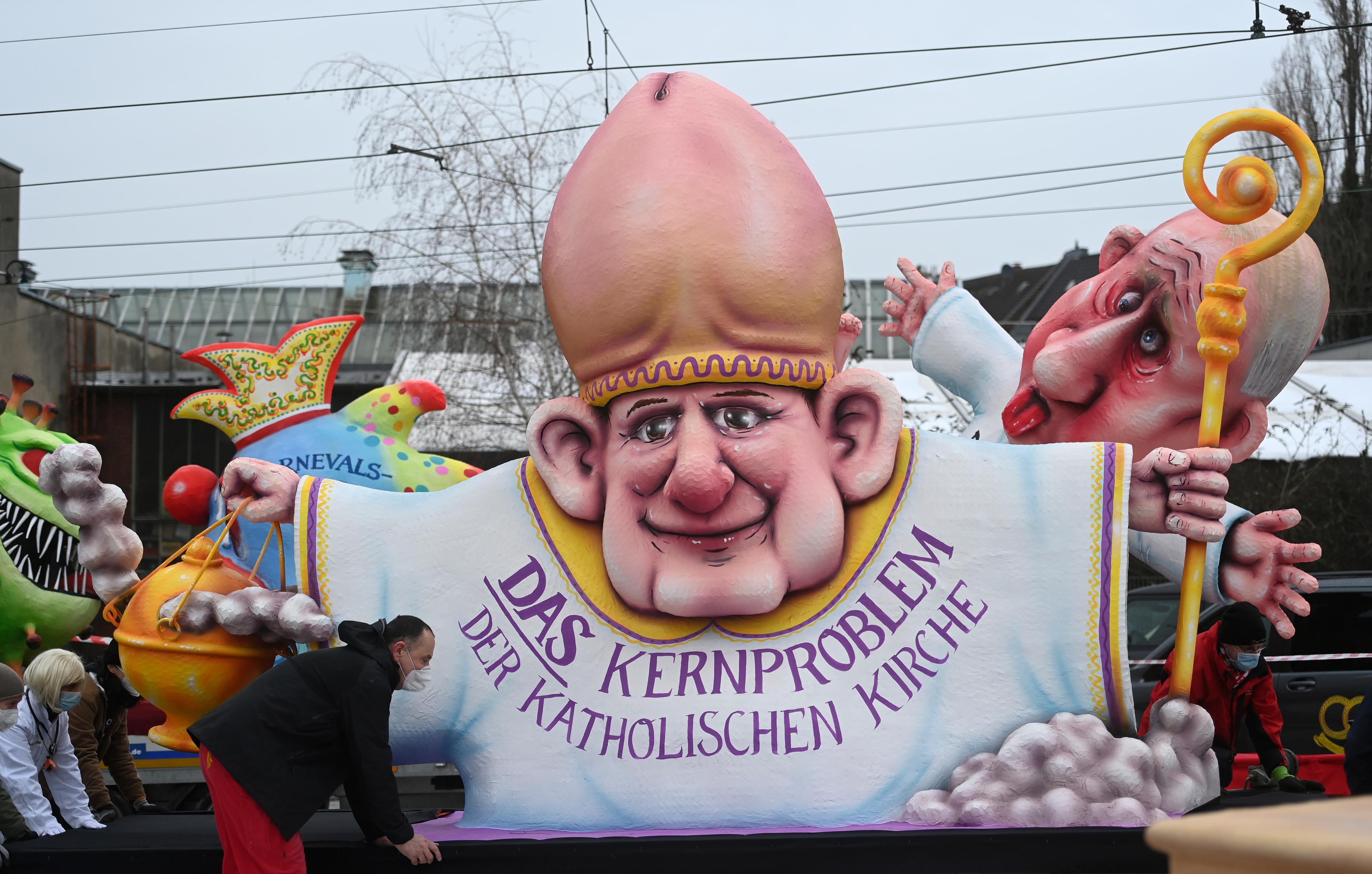 Helpers push a carnival float depicting a Catholic bishop wearing a glans penis-shaped mitra and wearing a robe that reads "The core problem of the Catholic Church" during a slimmed down version of the traditional Rose Monday parade on February 15, 2021 in Duesseldorf, western Germany. - Due to the novel coronavirus / COVID-19 pandemic, traditional parades and festivities in Germany's carnival hotspots, mainly situated in the Rhineland region, had to be canceled or modified to conform to the rules and restrictions in order to limit the spread of the virus. (Photo by Ina Fassbender / AFP)