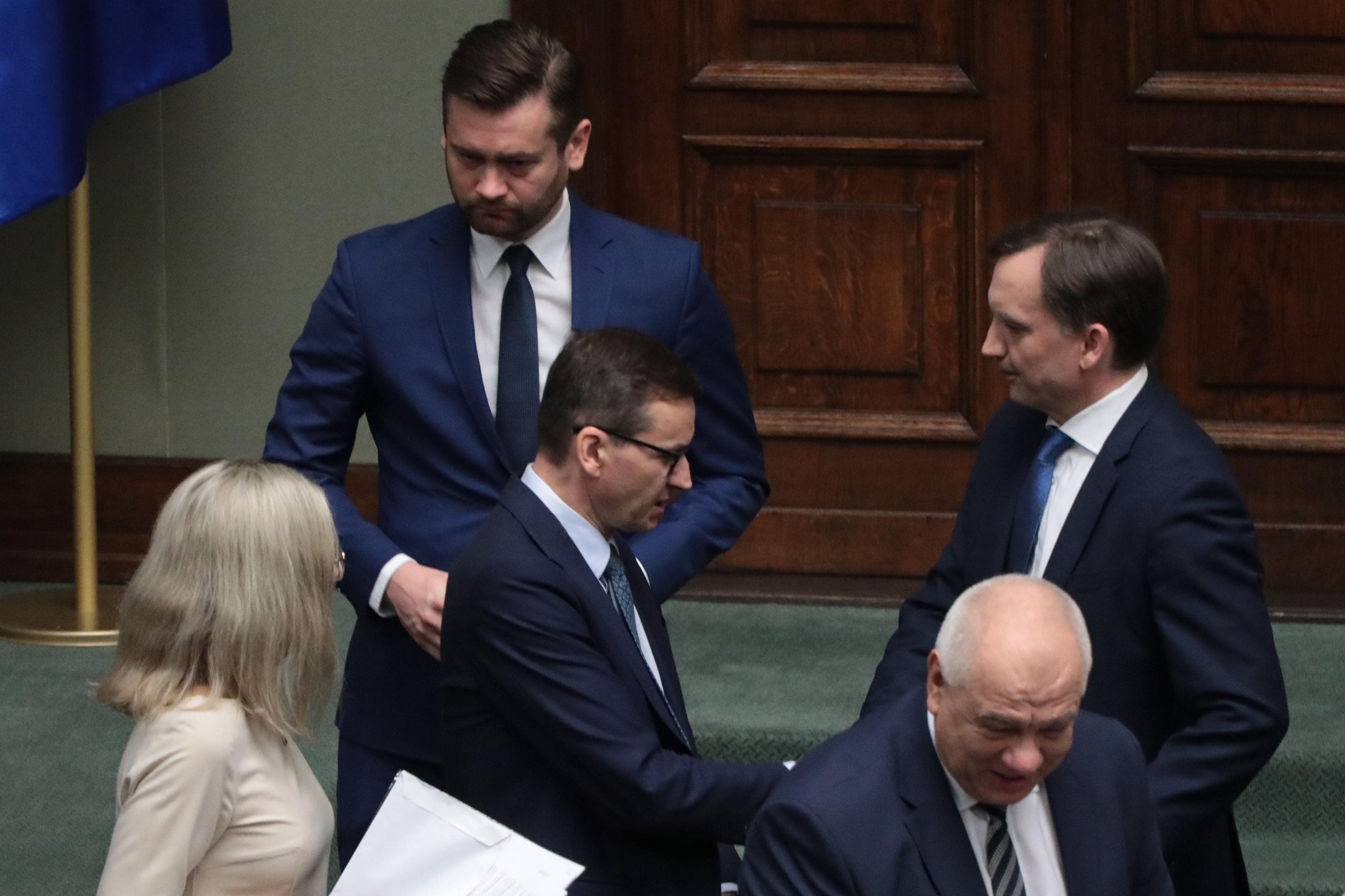 Ławy rządowe w Sejmie, stoją obok siebie mężczyźni w garniturach