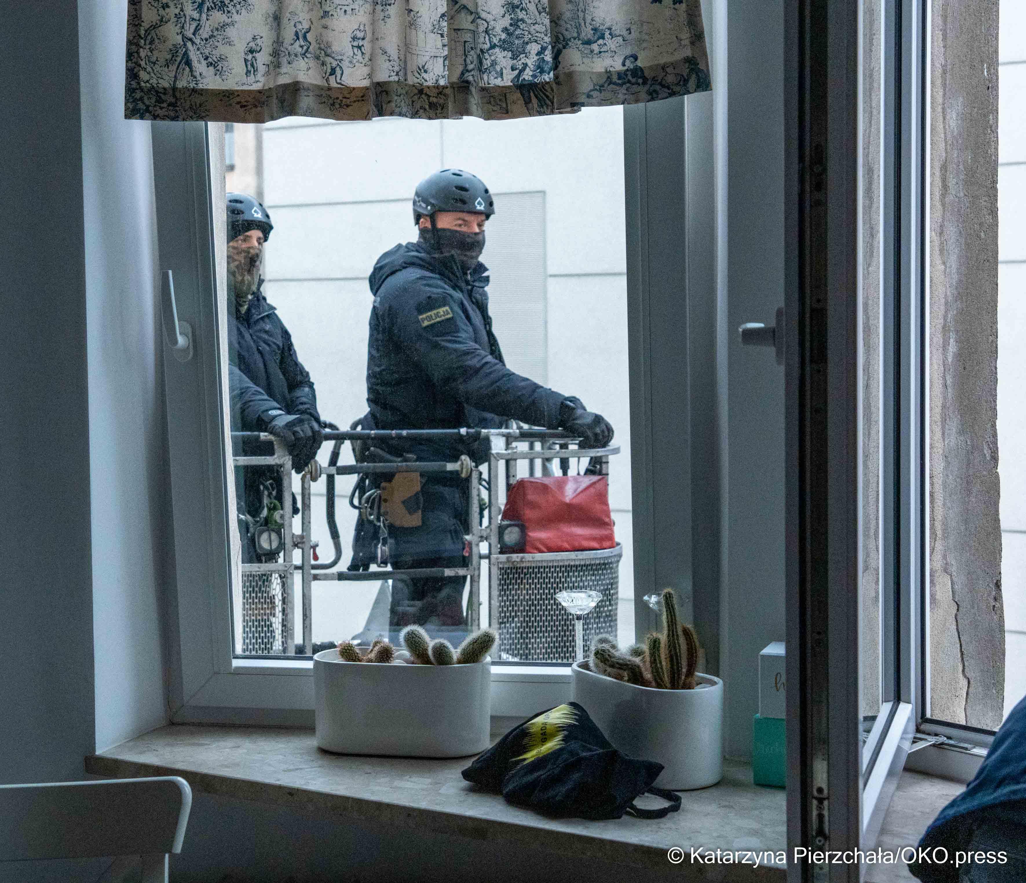 Dwóch policjantów widać przez okno, stoją na podnośniku