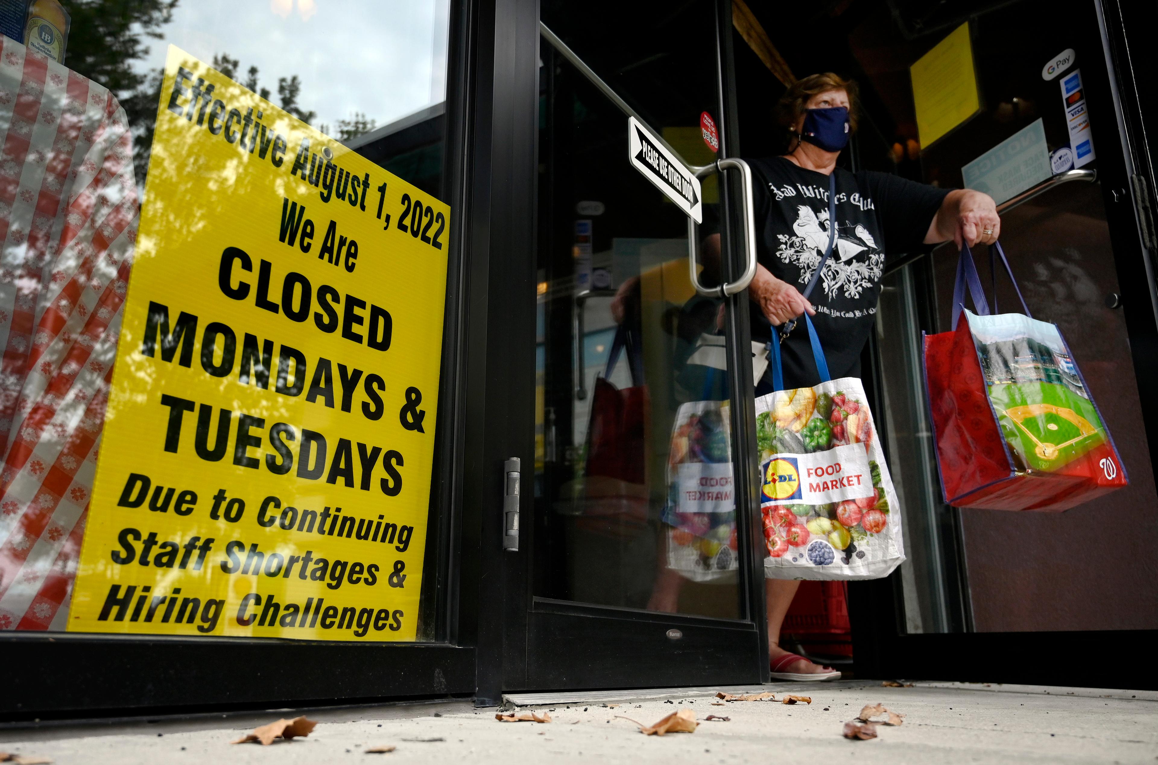 kobieta w maseczce wychodzi ze sklepu, na którym jest napis informujący o zamknięciu w poniedziałki i wtorki ze względu na brak pracowników