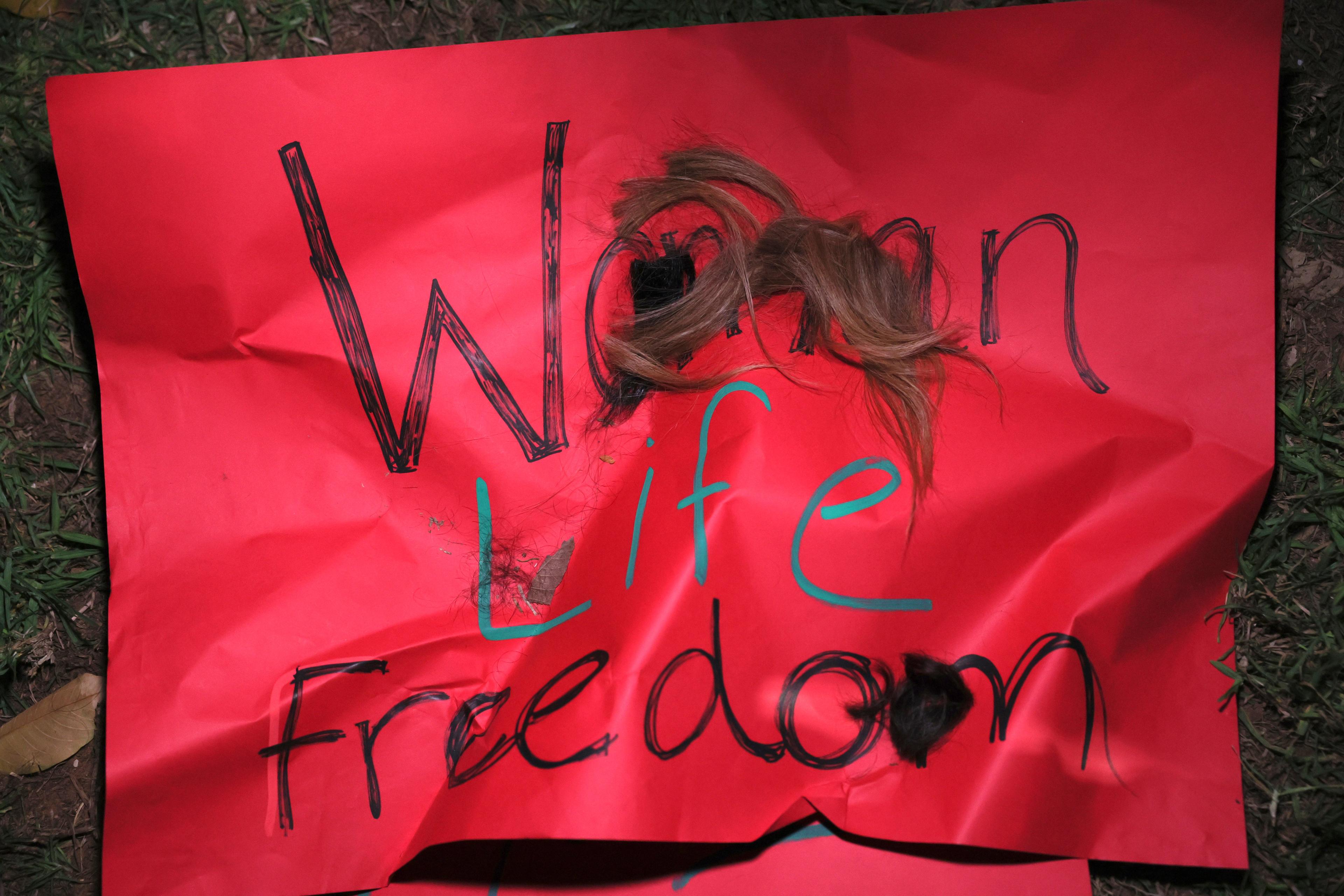 baner z napisem Women Life Freedom i uciętym puklem włosów