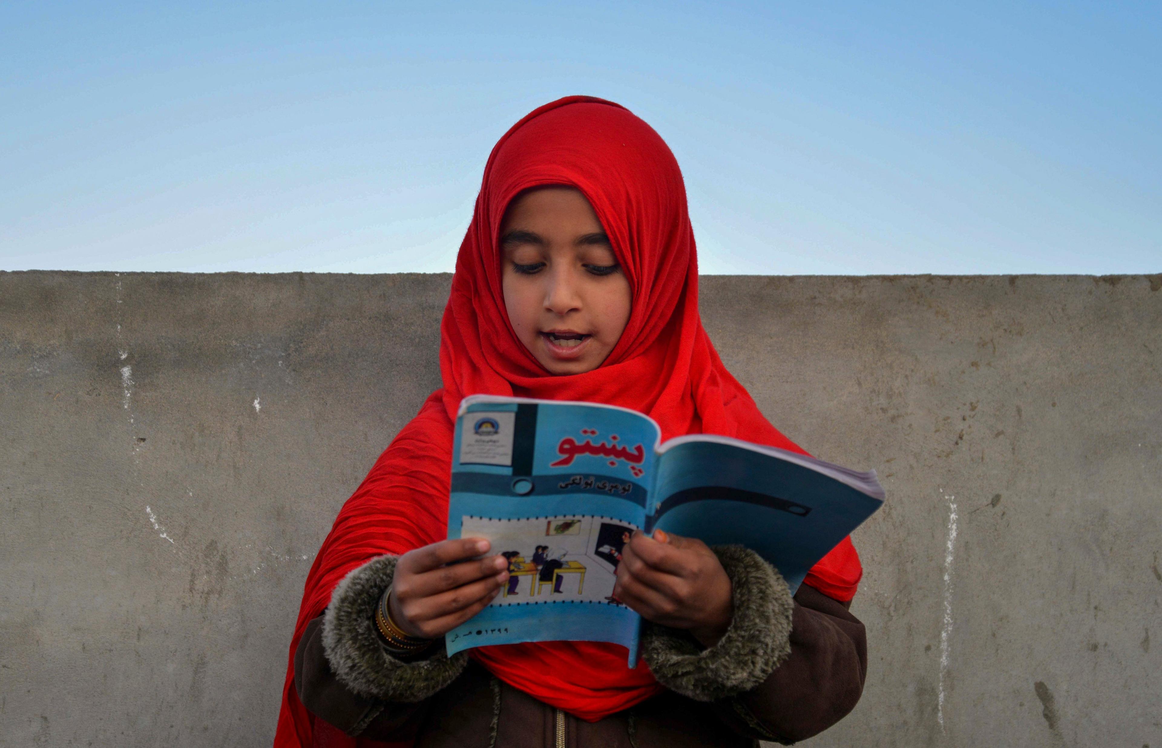 dziewczynka w czerwonym hidżabie czyta podręcznik