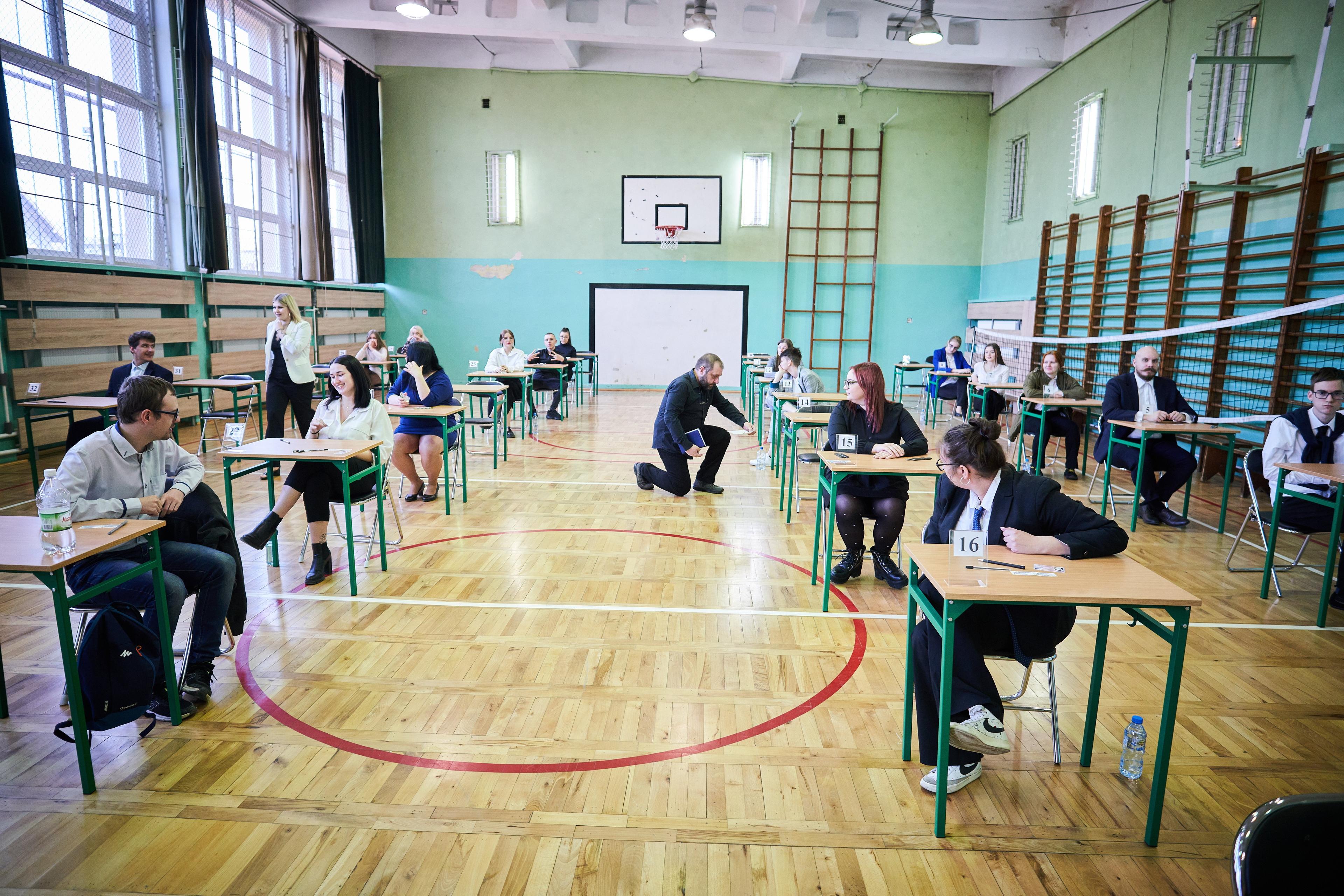 Na zdjęciu: Uczniowie w galowych strojach na sali gimnastycznej, podchodzący do egzaminu dojrzałości
