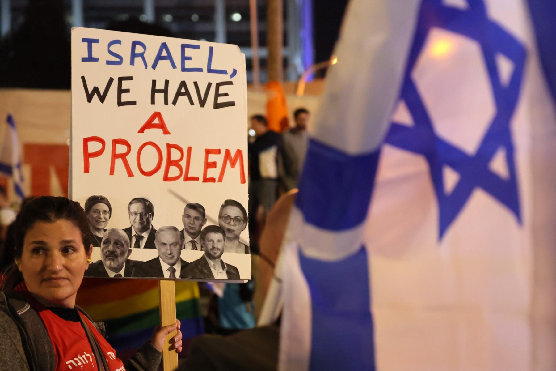 W tle tłum,. na pierwszym planie kobieta z banerem "Israel, we have a problem"