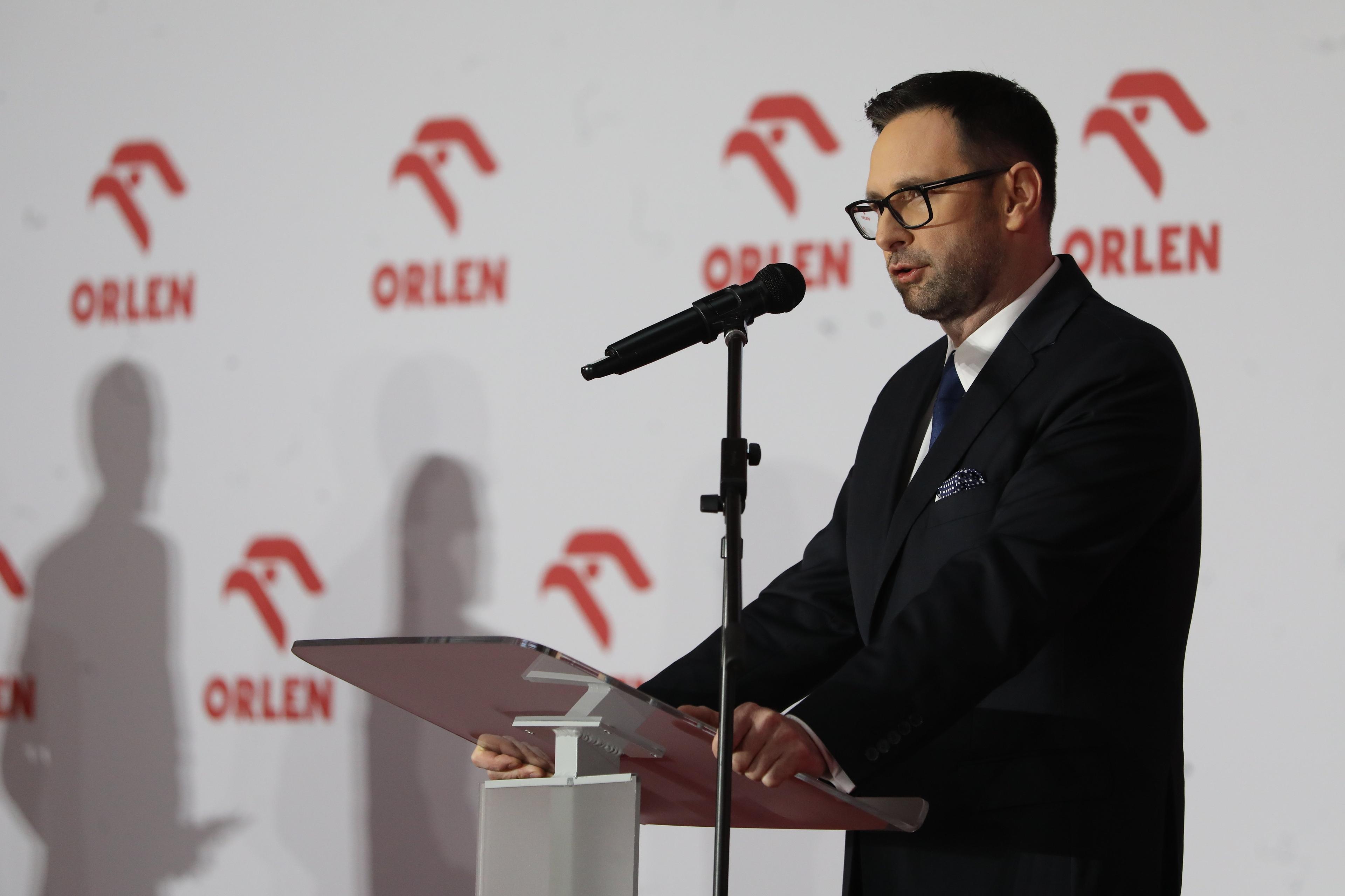 prezes Orlenu Daniel Obajtek przemawia na tle ścianki z logiem koncernu