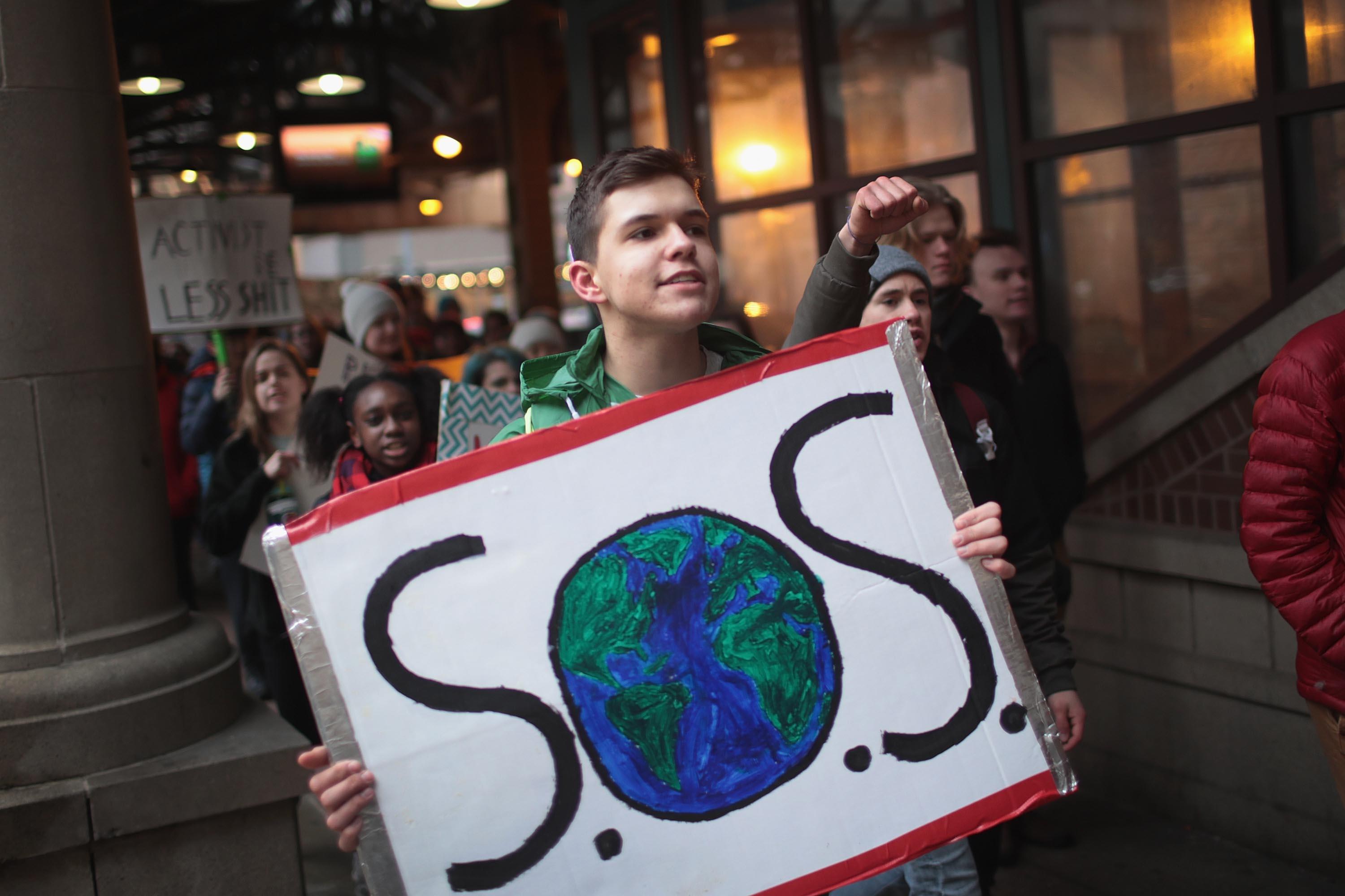 chłopiec trzyma plakat z rusunkiem kuli ziemskiej, wpisanej w litery S.O.S.