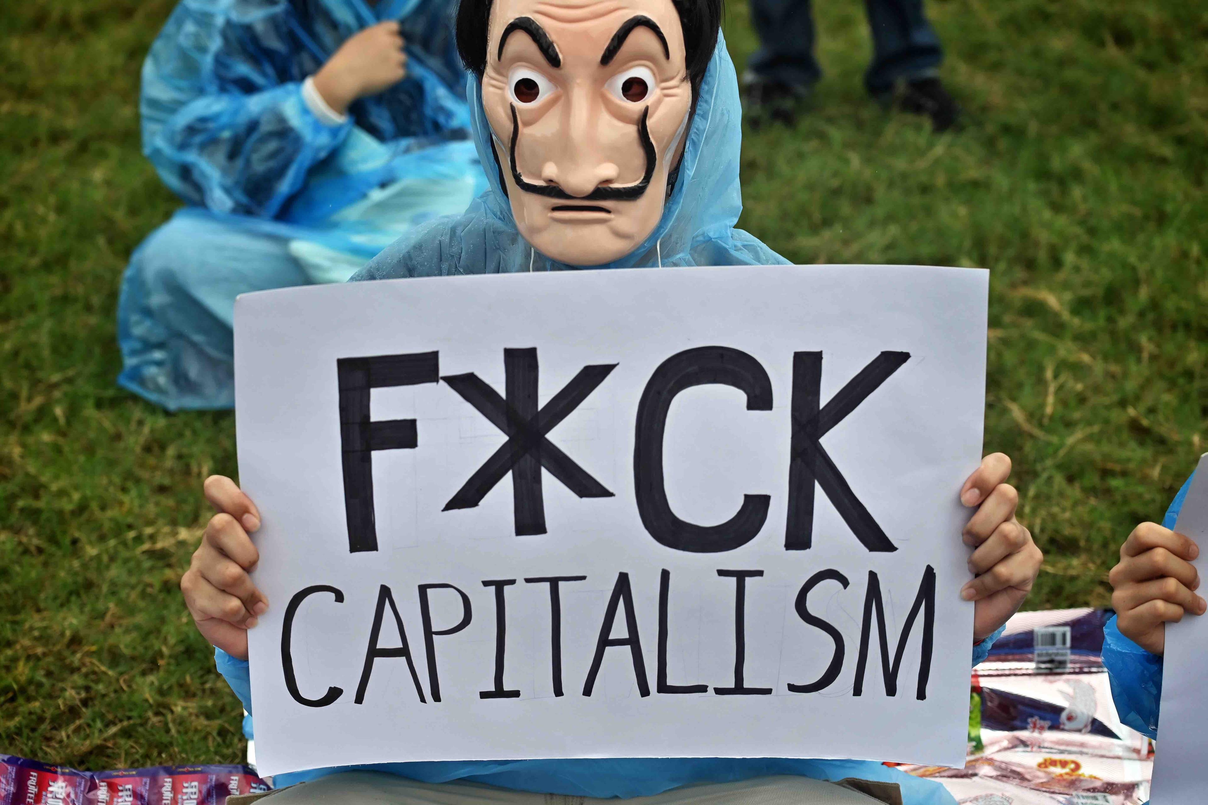 demonstrant w masce z komiksu V jak vendetta trzyma karton z hasłem Fuck capitalism