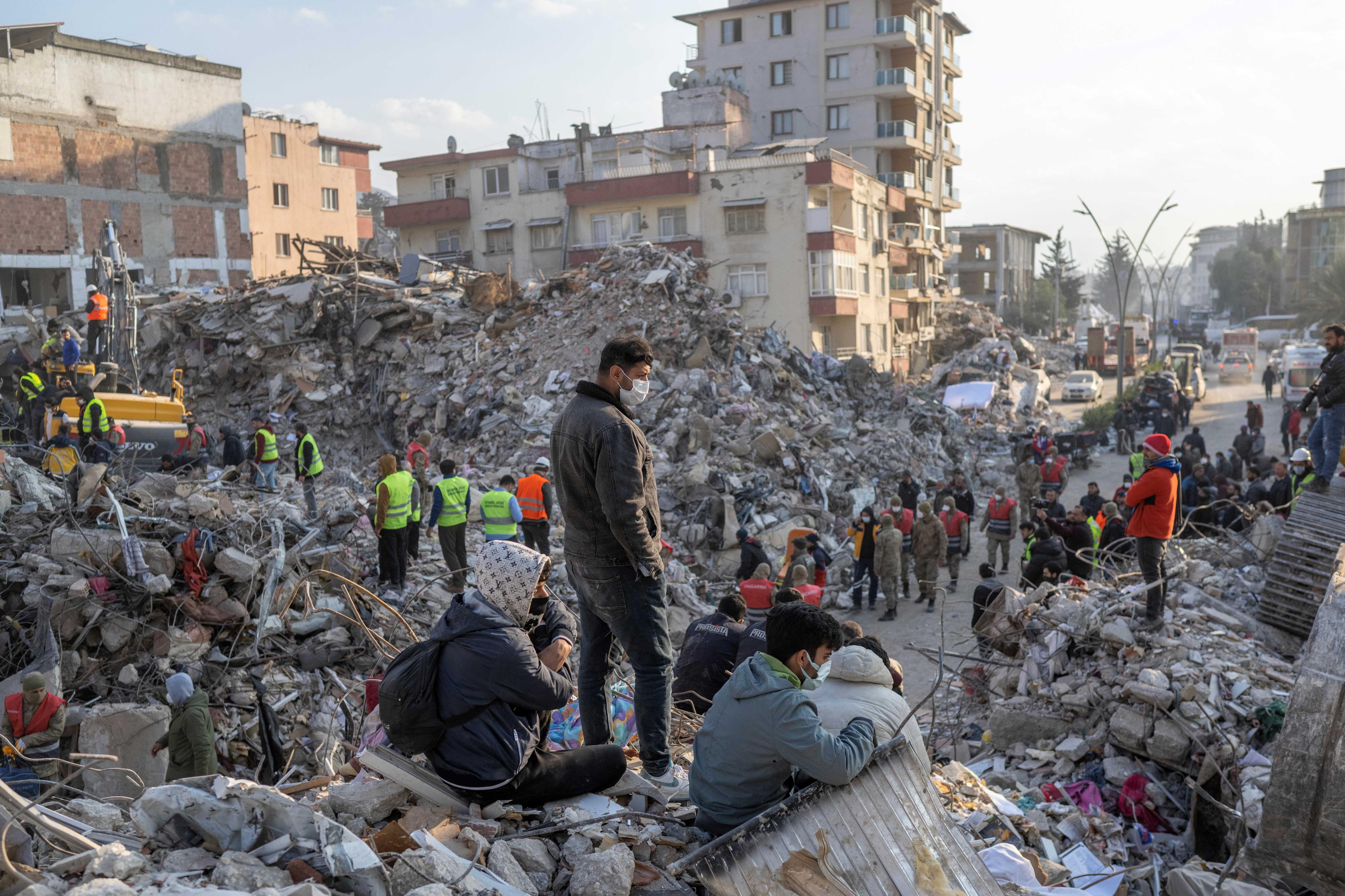 People stand on top of rubble of collapsed buildings during rescue operations  in Hatay on February 12, 2023, after a 7,8 magnitude earthquake struck the border region of Turkey and Syria earlier in the week. (Photo by BULENT KILIC / AFP)