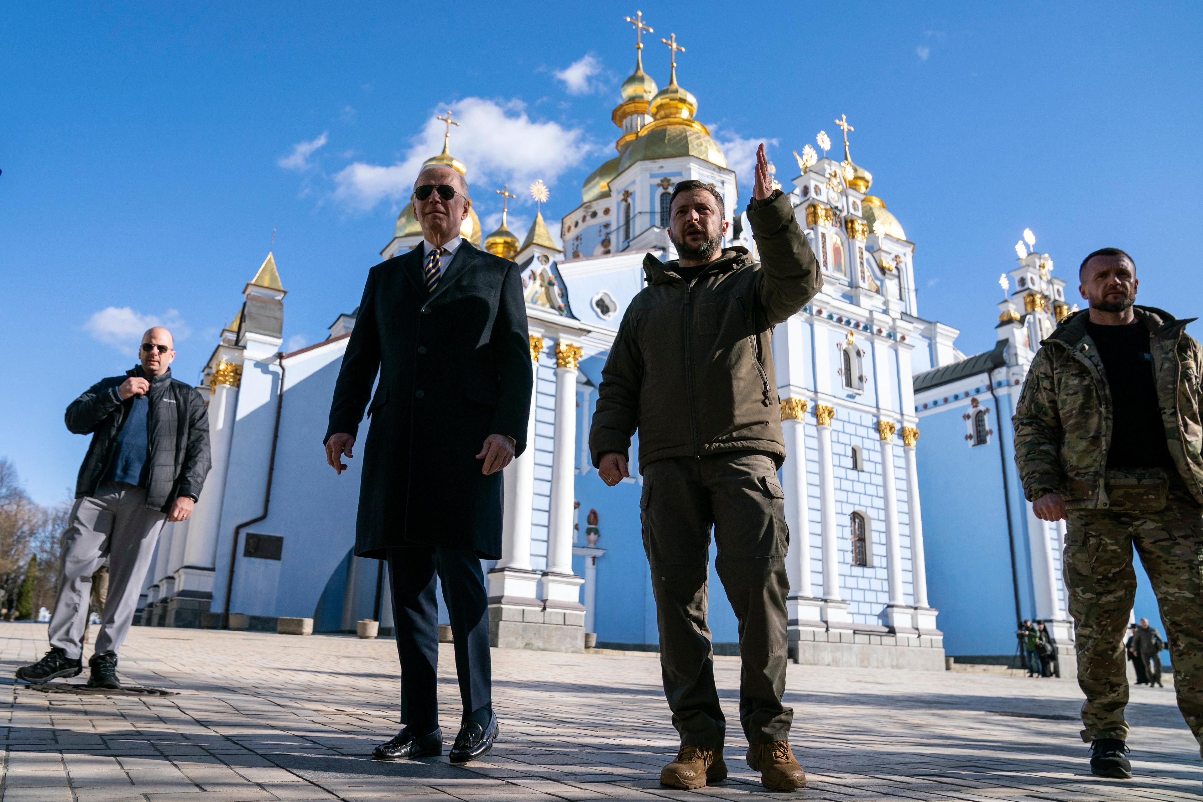 dwaj mężczyźni stoją na placu na tle błękitnego nieba i jasnej cerkwii ze złoconym dachem. To Joe Biden i Wołodymyr Zełenski