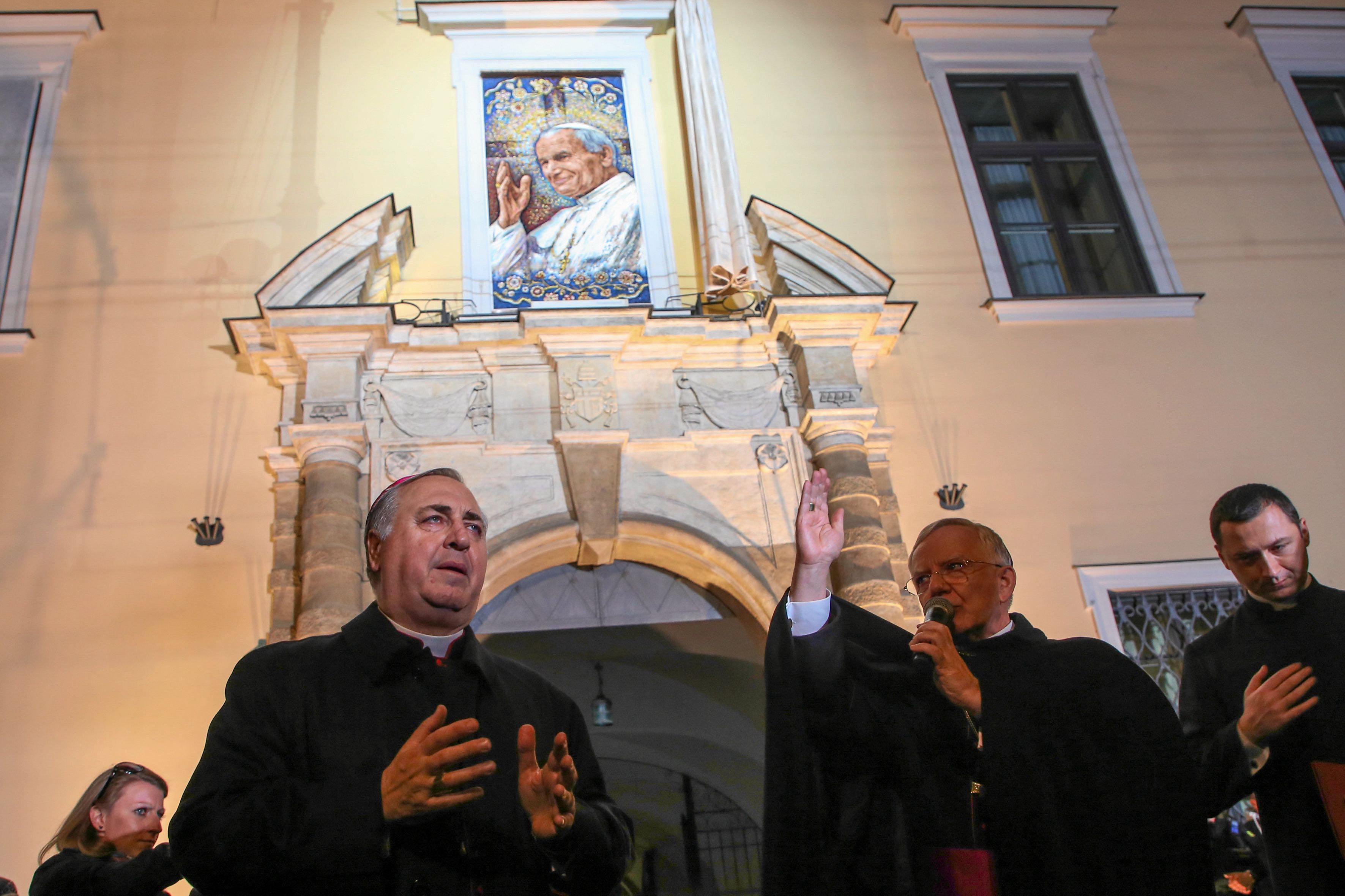 dwaj duchowni katoliccy modlą się pod budynkiem krakowskiej kurii, na którym jest podobizna papieża Jana Pawła II