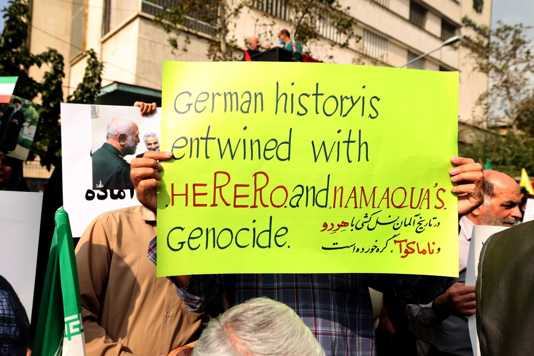Protest przed ambasadą Niemiec - protestant trzyma baner z napisem, że historia Niemiec jest związana z mordami na ludach Herero i Namu