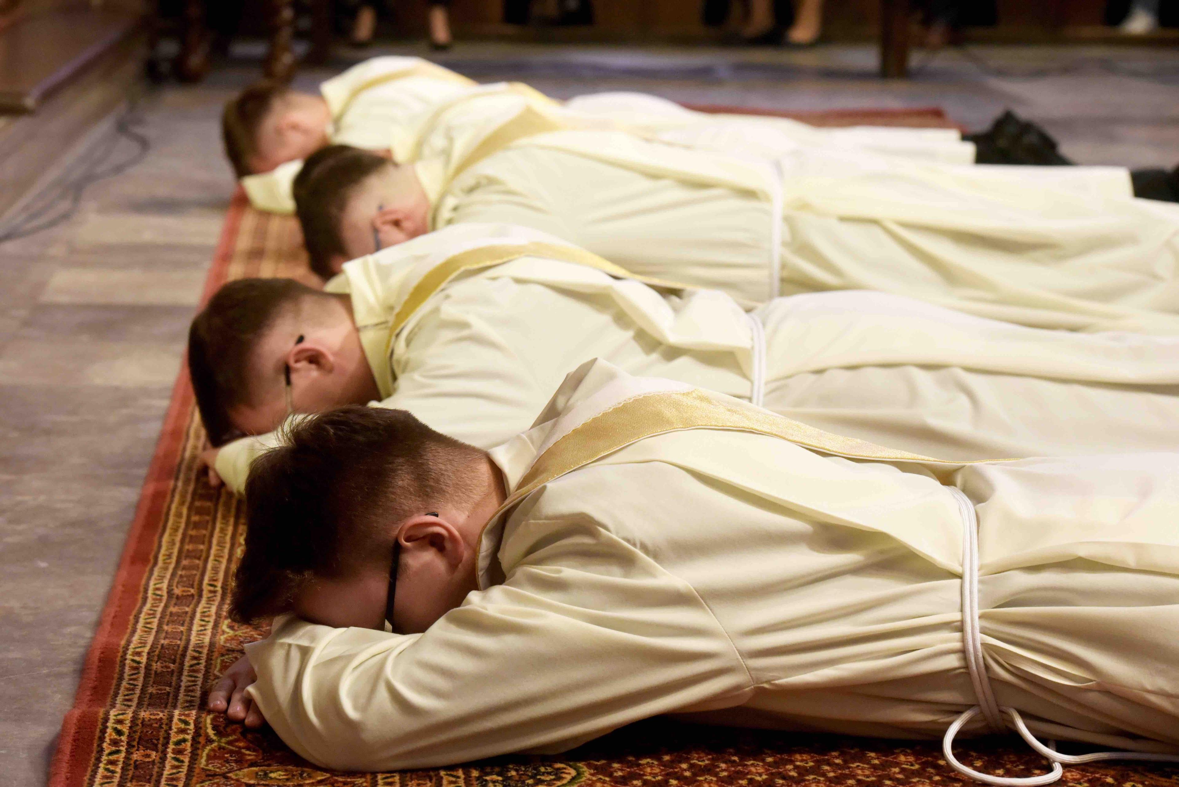 klerycy w białych szatach modlą się, leżąc na posadzce kościoła