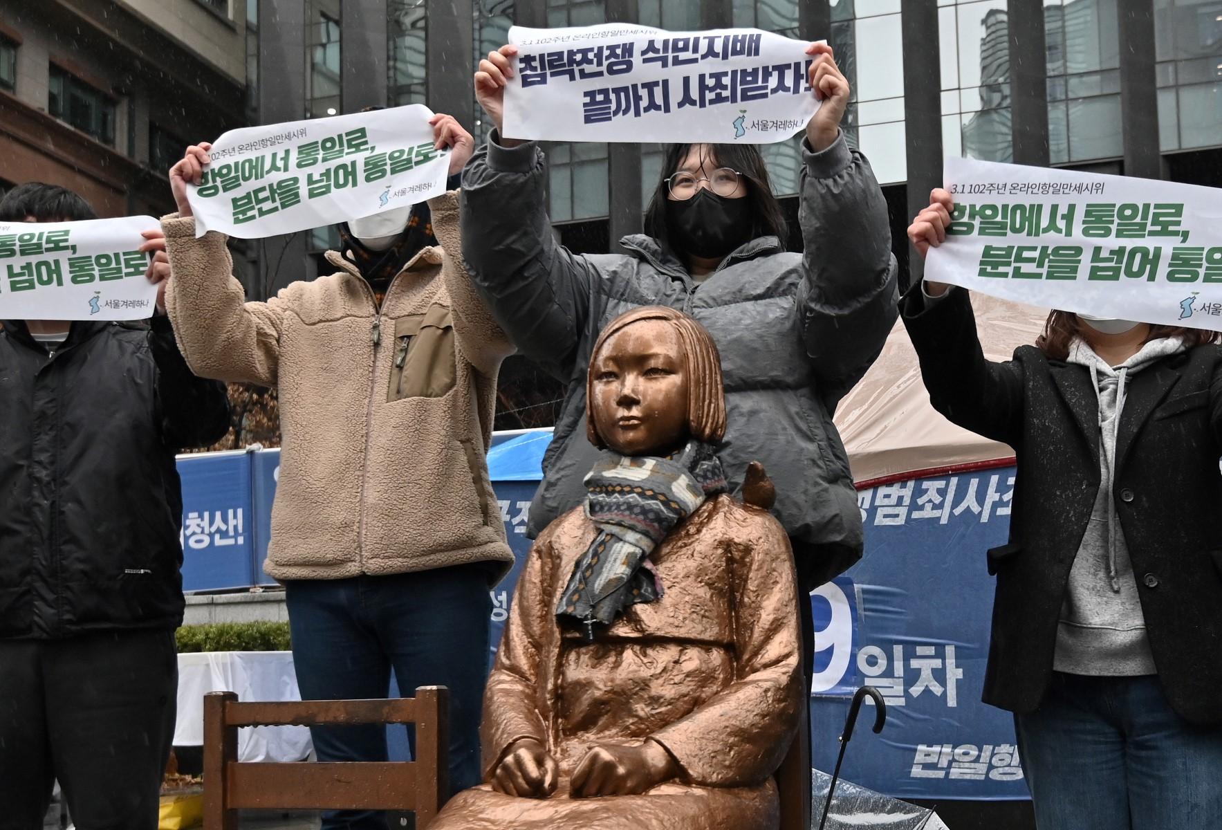 South Korean protesters hold up banners beside a statue (C) of a teenage girl symbolising "comfort women", who served as sex slaves for Japanese soldiers during World War II, near the Japanese embassy in Seoul on March 1, 2021, the 102nd anniversary of the Independence Movement Day against the 1910-1945 Japanese colonial rule. (Photo by Jung Yeon-je / AFP)