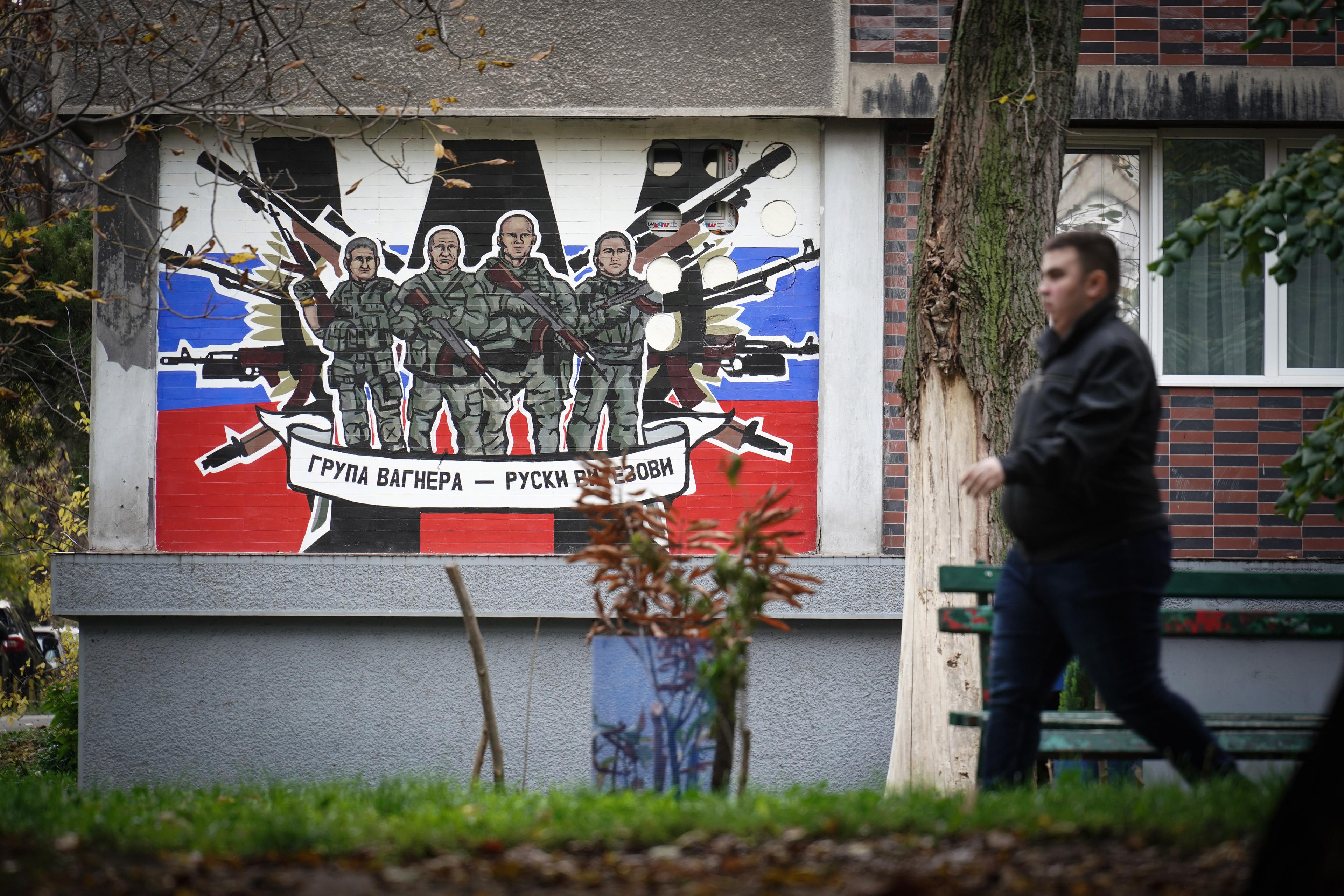 Czlowiek przechodzi koło domu z muralem w barwach Rosji. Serbski napis głosi "Grupa Wagnera - rosyjscy rycerze"