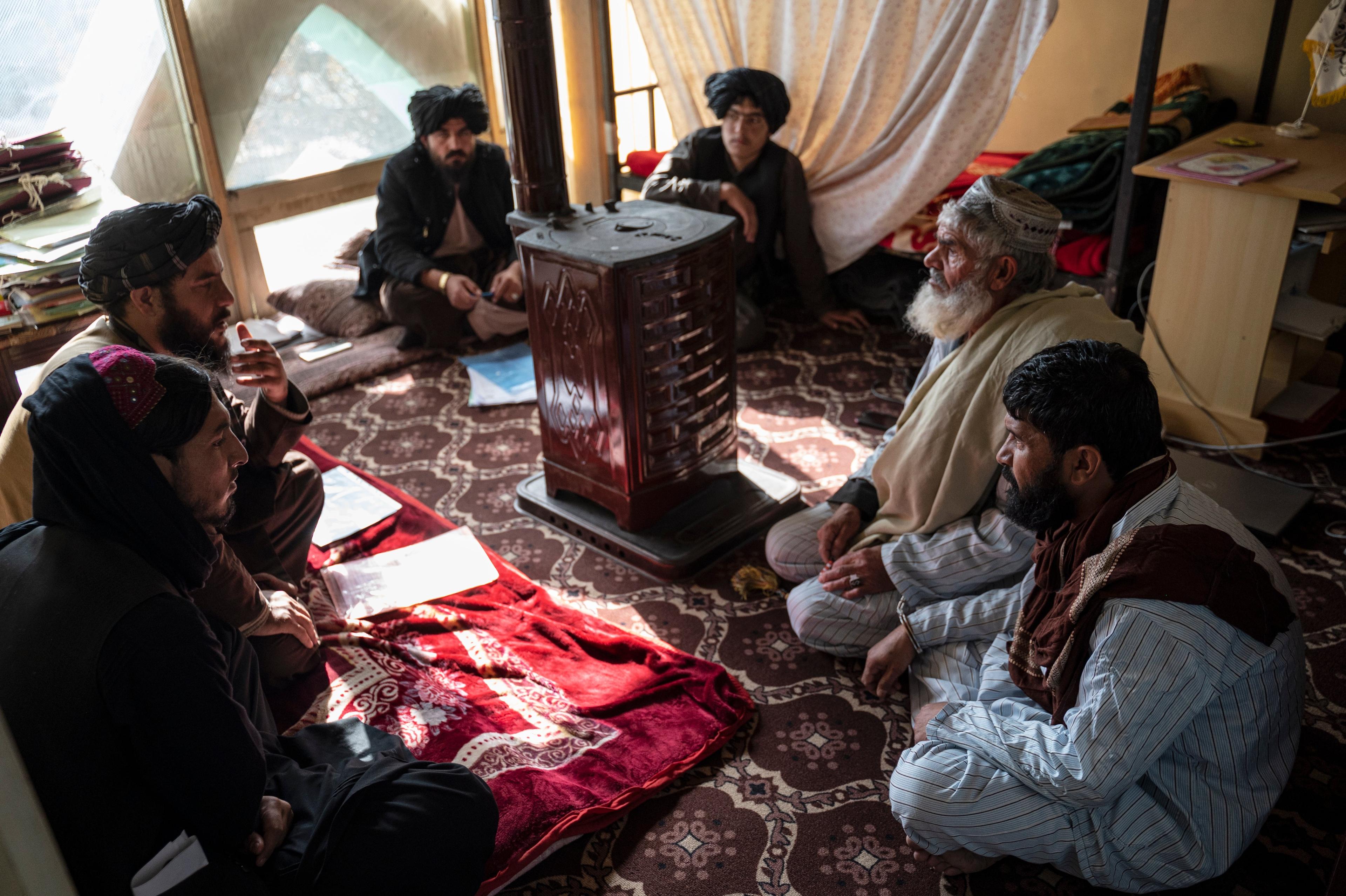 Mężczyźni w turbanach siedzący na podłodze w małym pomieszczeniu sądu w Afganistanie
