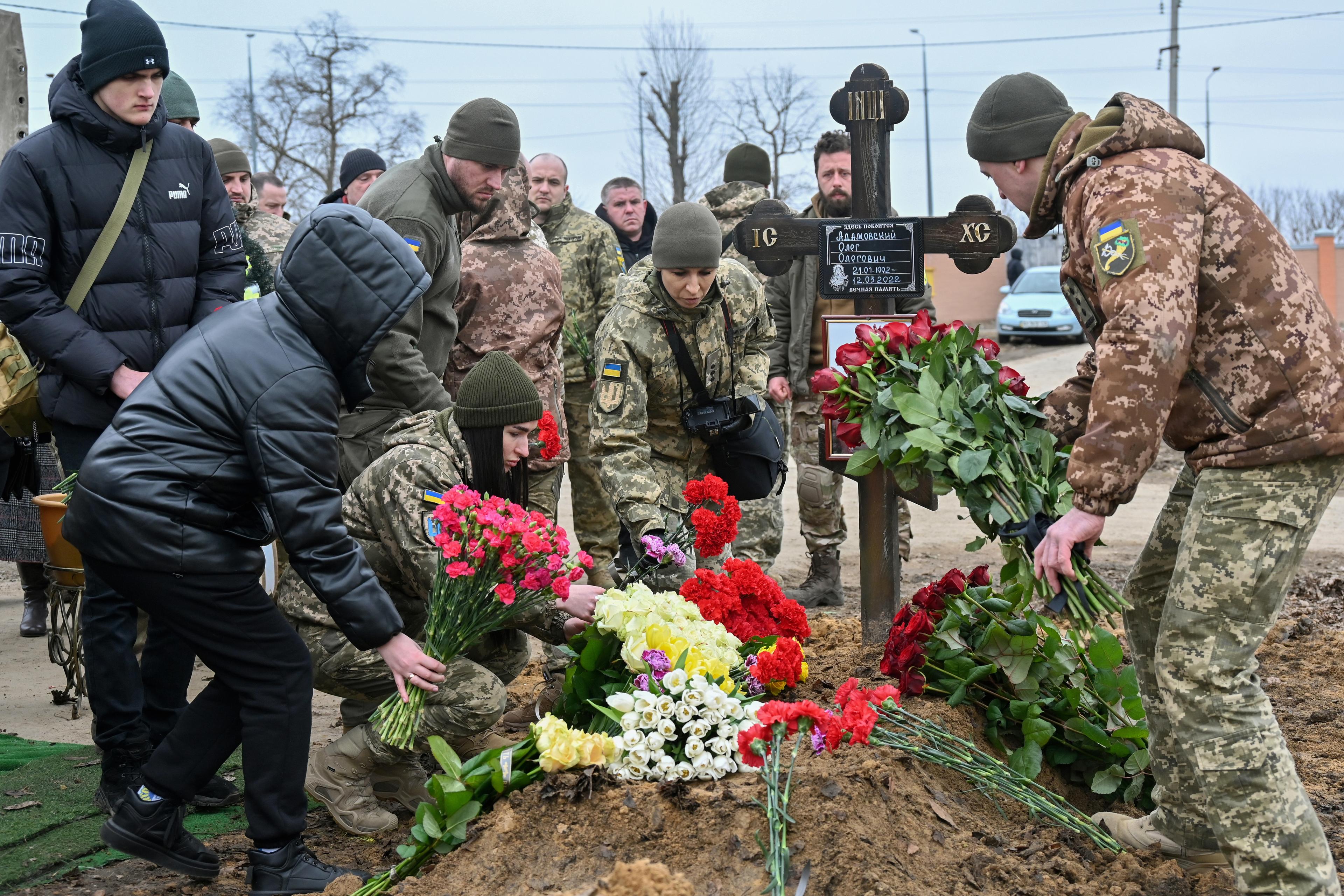 żołnierze i cywile kładą wieńce na świeżym grobie
