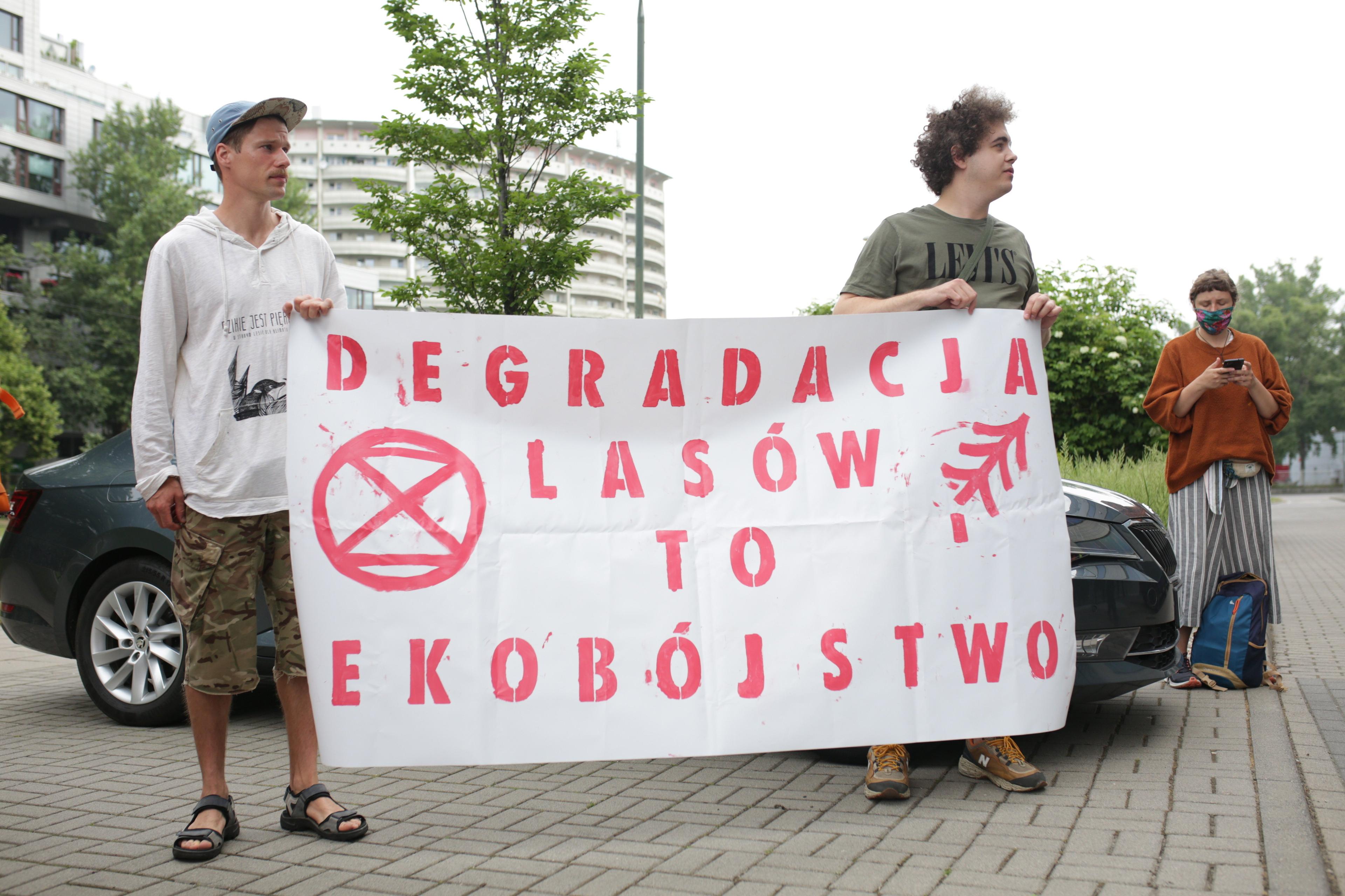 dwóch młodych mężczyzn z transparentem Degradacja lasów to ekobójstwo
