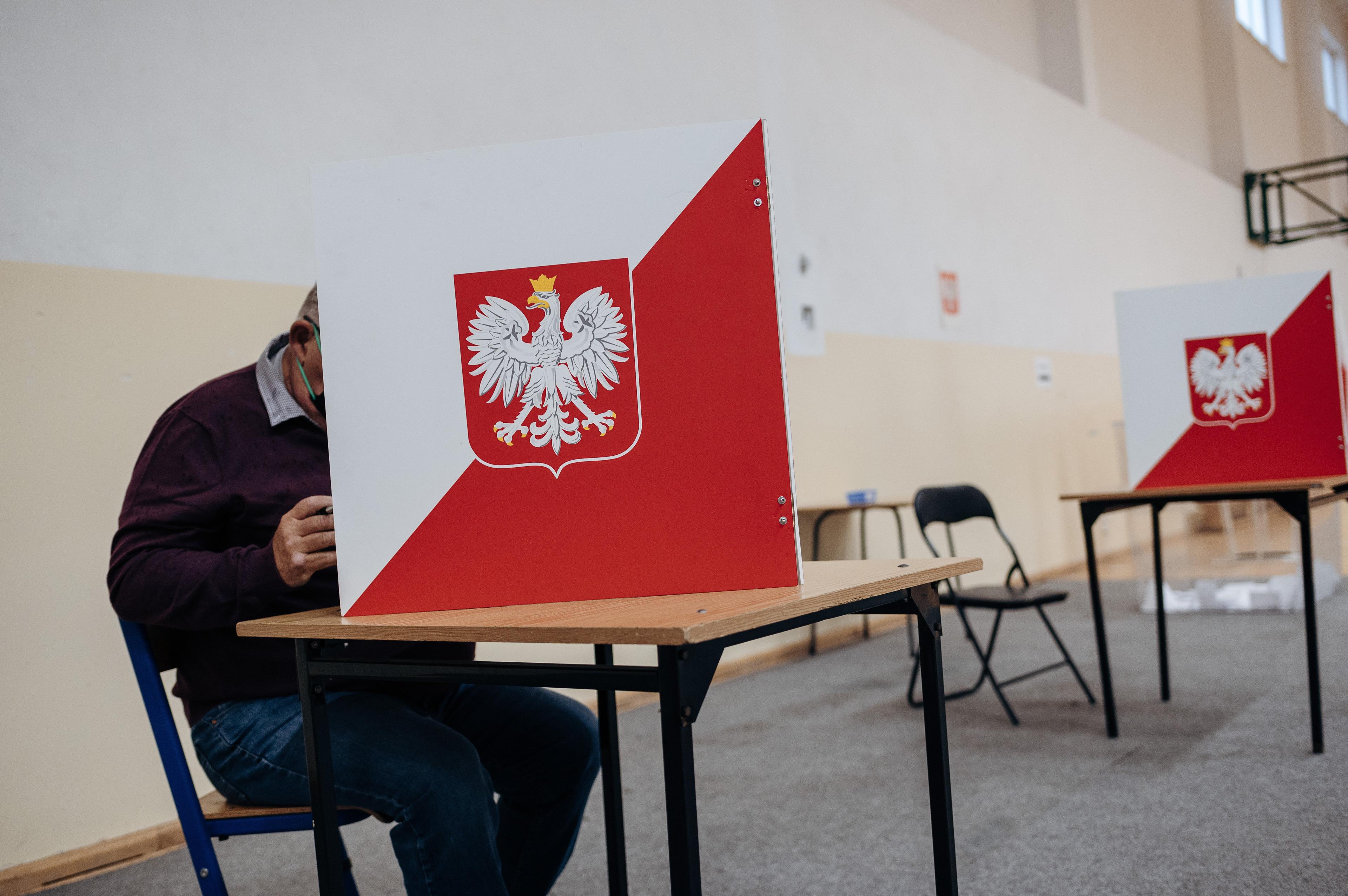 Mężczyzna głosujący w lokalu wyborczym, na pierwszym planie godło Polski
