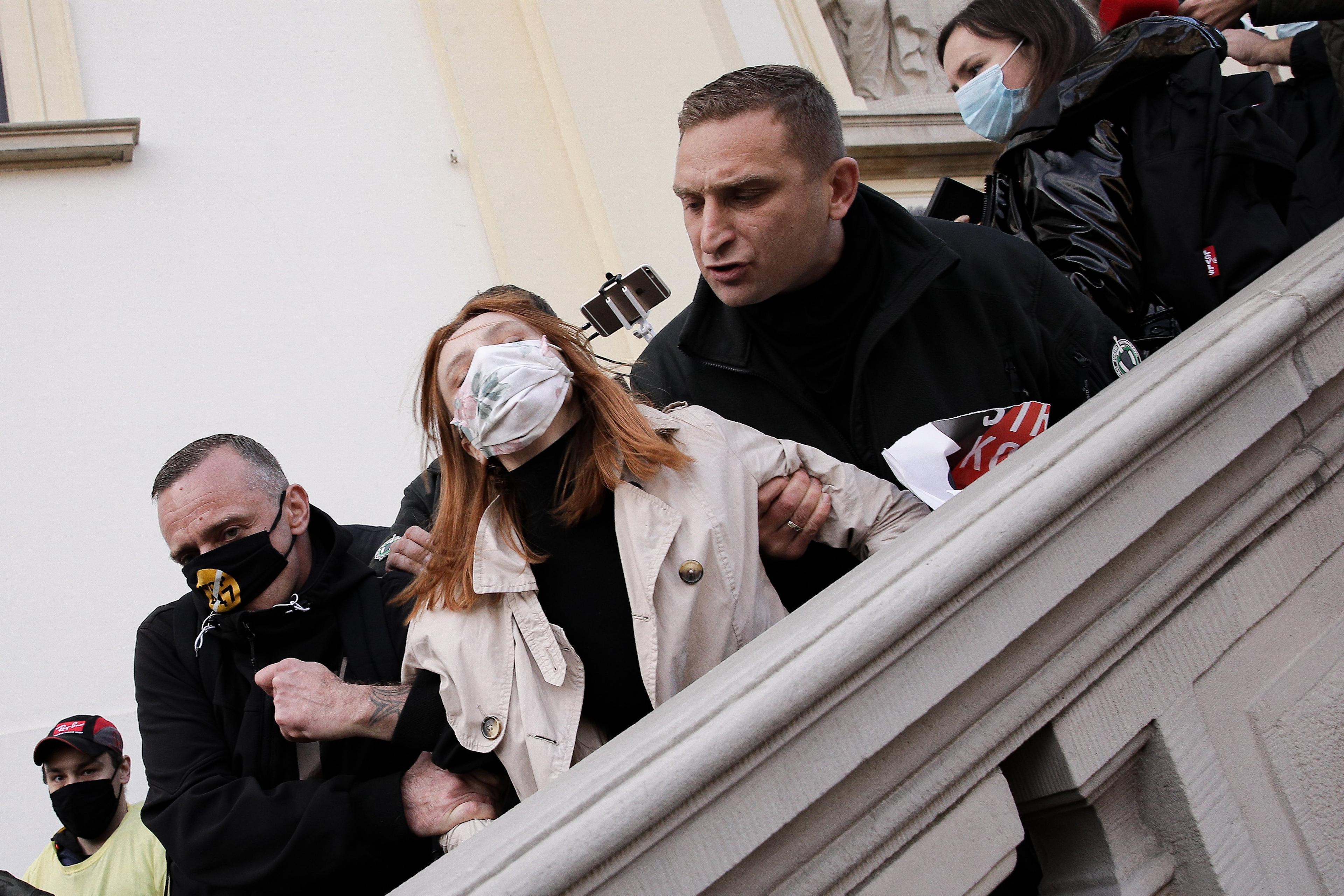 Mężczyzna w czerni (Robert Bąkiewicz) sprowadza ze schodów przed kościołem św. Krzyża w Warszawie kobietę w maseczce