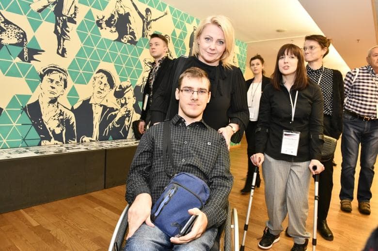 Kobieta z mężczyzną na wózku wśród ludzi w kuluarach dużej imprezy