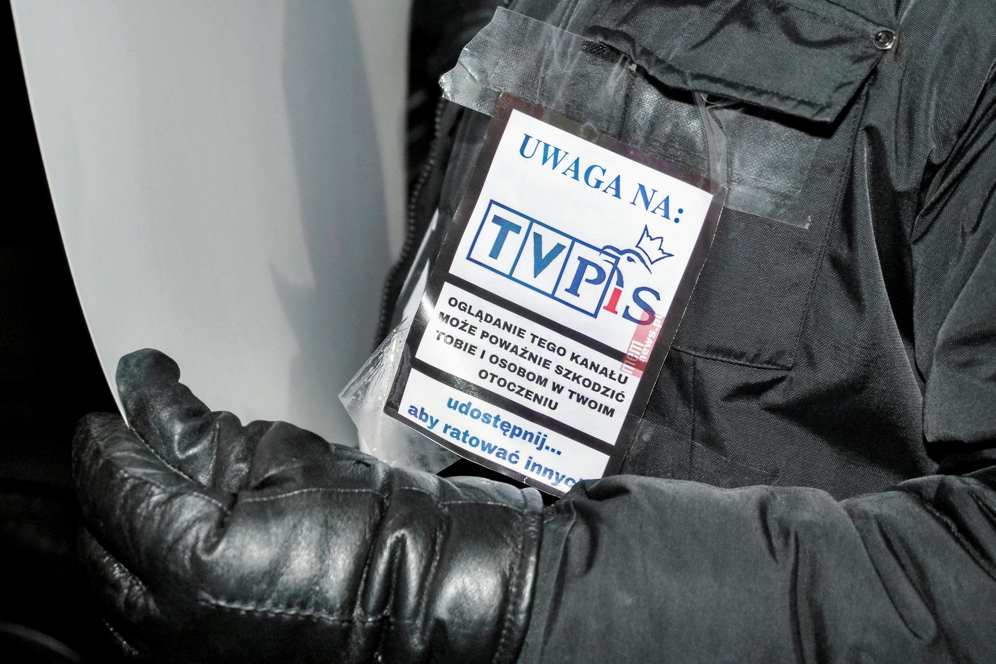 Plakietka z napisem "Uwaga na TVP" przypięta na zimowej kurtce
