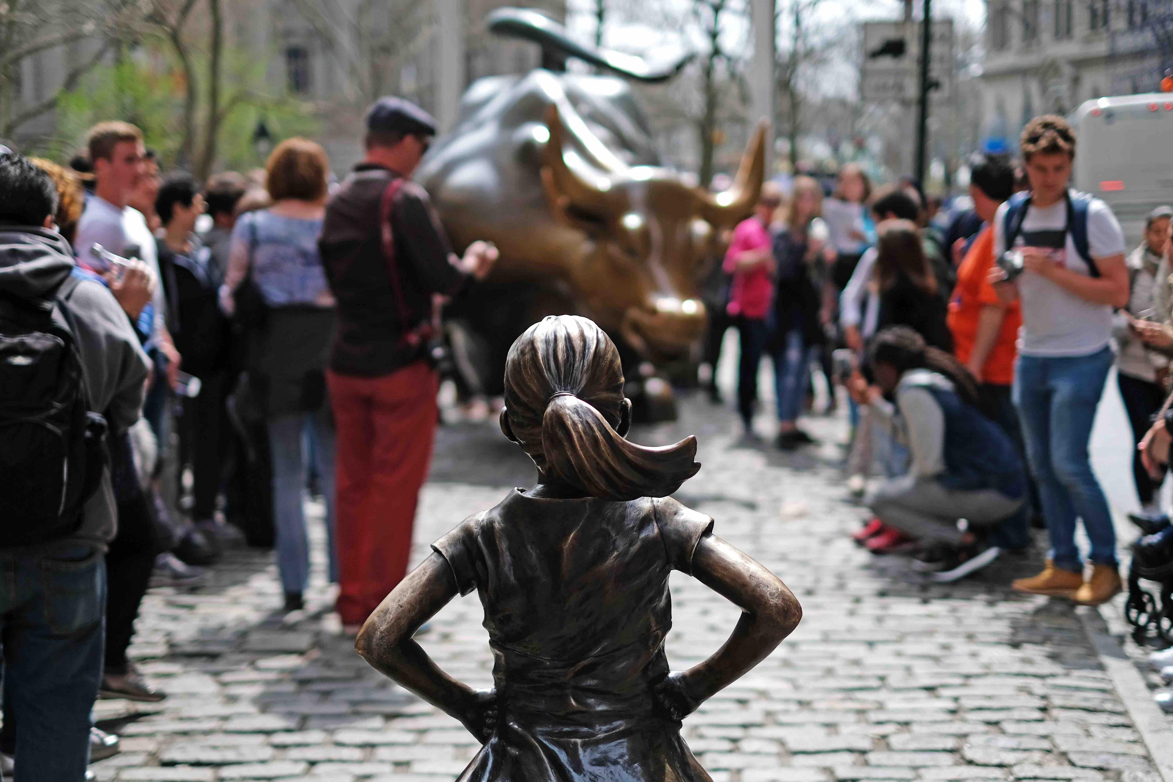 Ustawiona na placu Instalacja artystyczna, przedstawiająca figurę dziewczynki, która stoi na drodze szarżującego byka. Dookoła stoją ludzie i robią zdjęcia.
