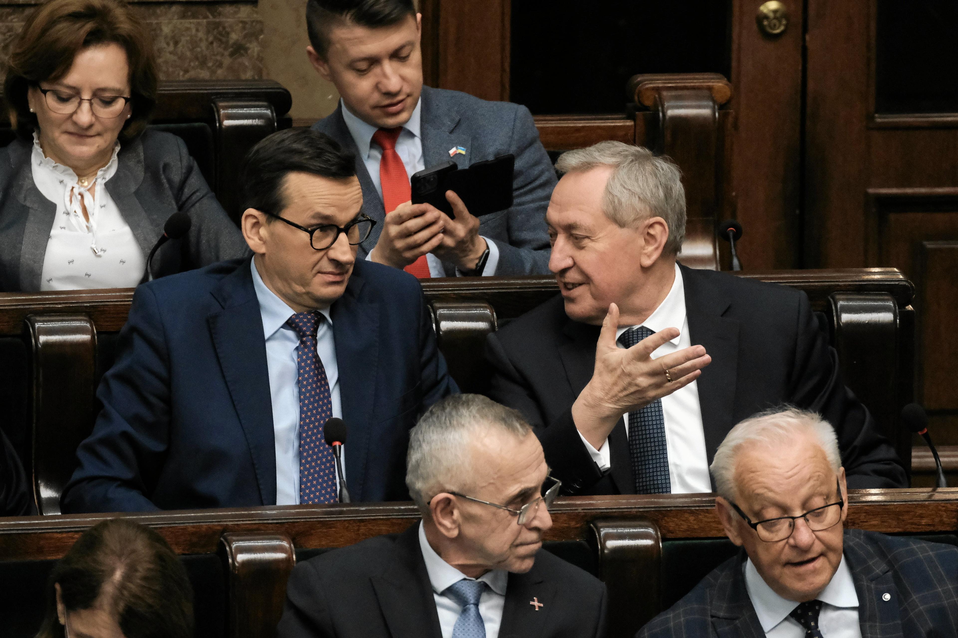 Mężczyźni w garniturach w ławach rządowych w Sejmie. Premier Mateusz Morawiecki robi zdziwioną minę, a minister Henryk Kowalczyk gestykuluje