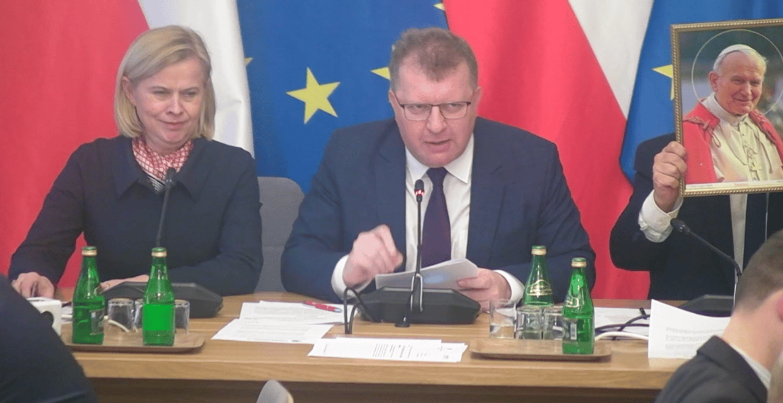 posłowie na tle flag UE i Polski, jeden zasłania się