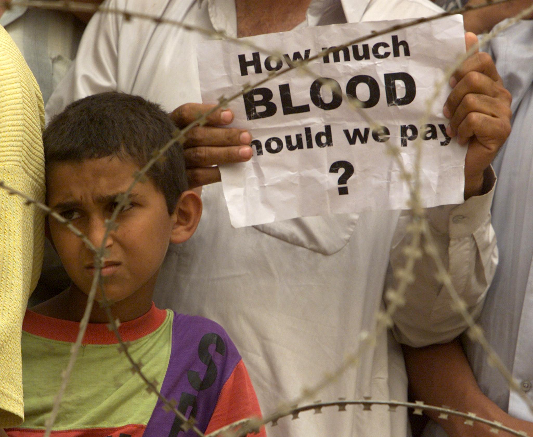 mężczyzna trzyma kartkę z napisem „How much blood should we pay?", obok stoi dziecko