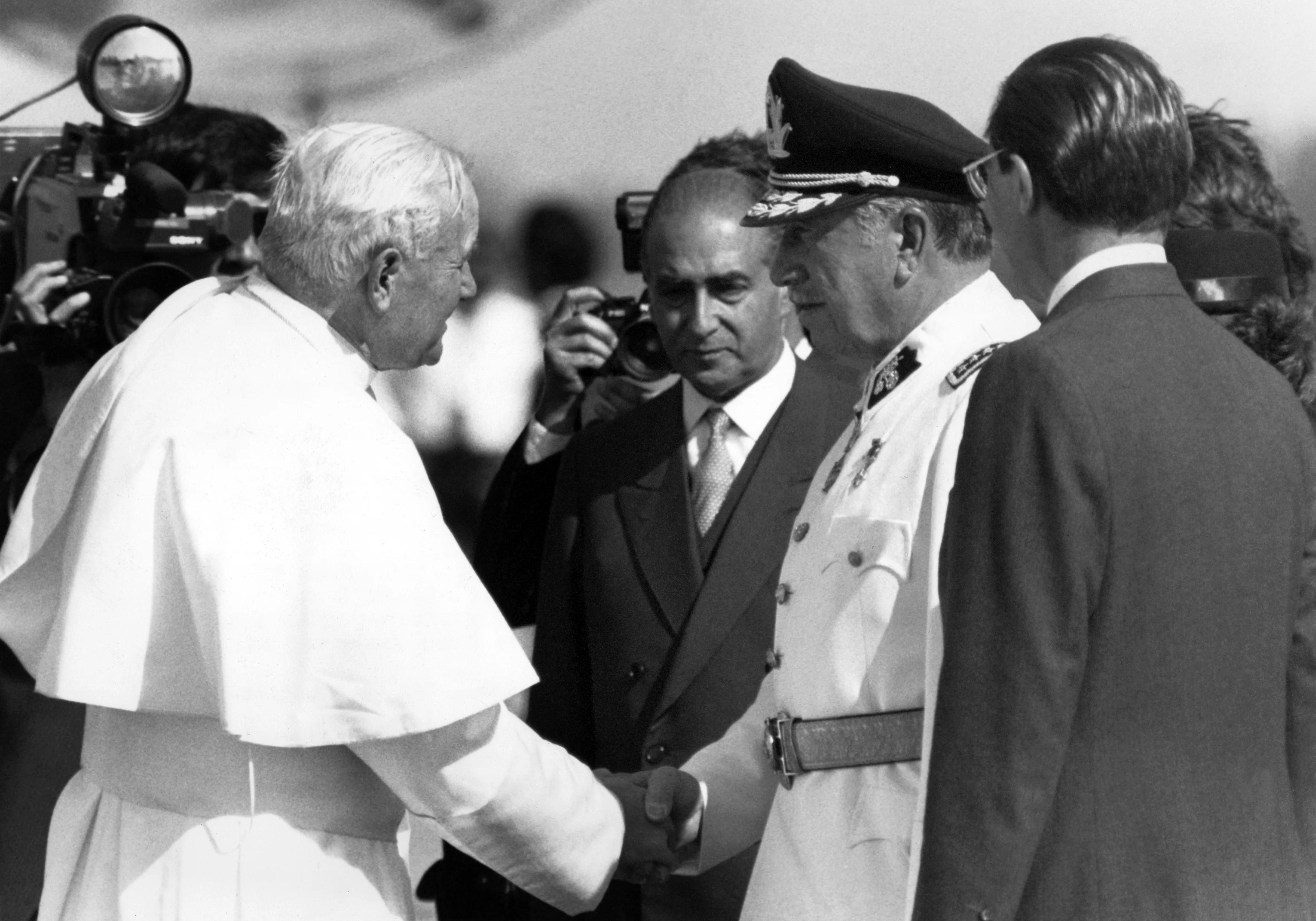 Papież Jan Paweł II ściska rękę dyktatora Chile Augusto Pinocheta, w otoczeniu urzędników w garniturach.